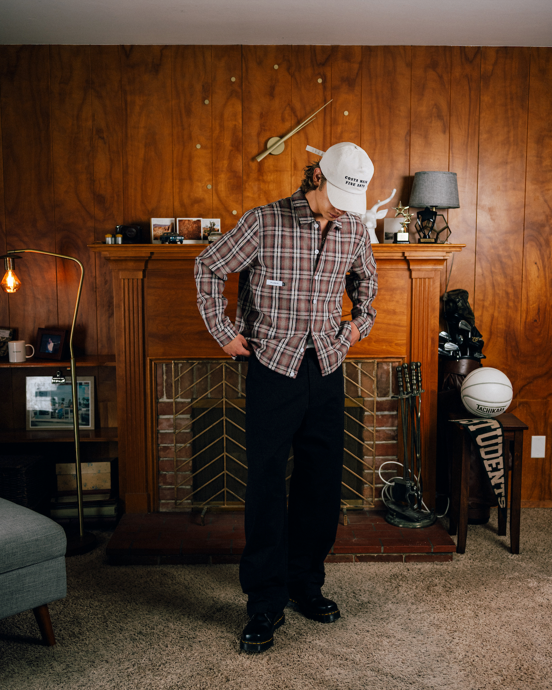 Person wearing a plaid shirt and white cap in a room with wooden walls and furniture.