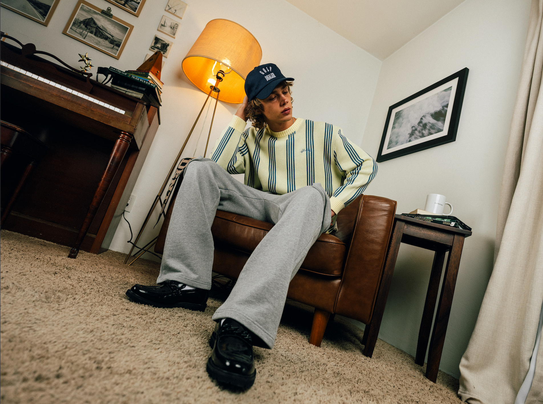 Person sitting on a leather chair in a room with a lamp and framed pictures.
