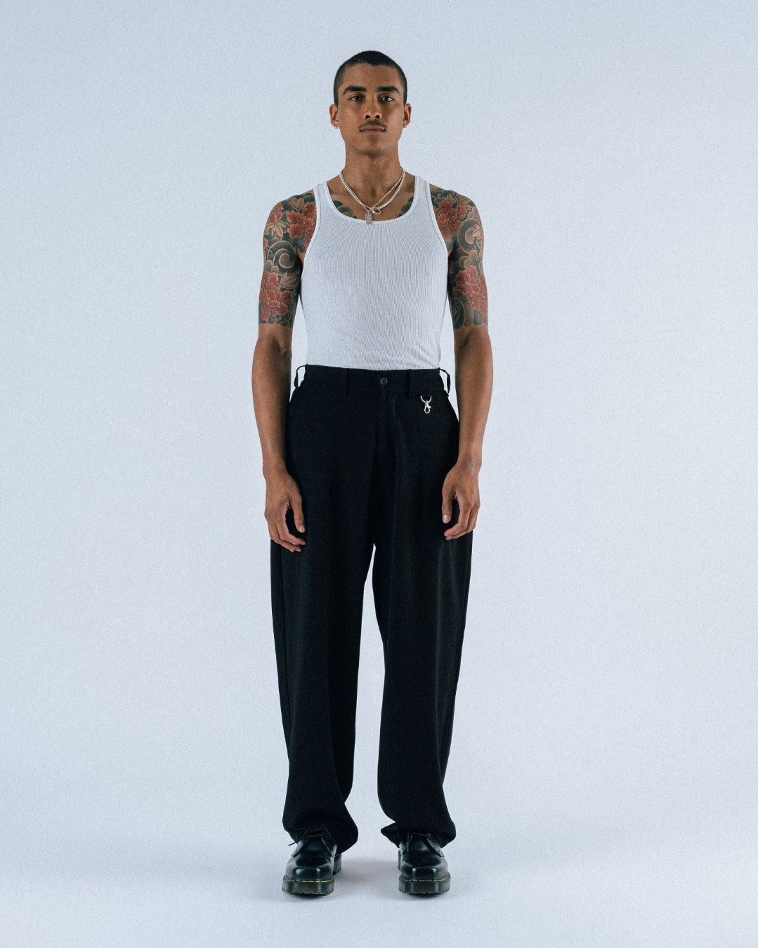 Person wearing a white tank top and black pants on a white background