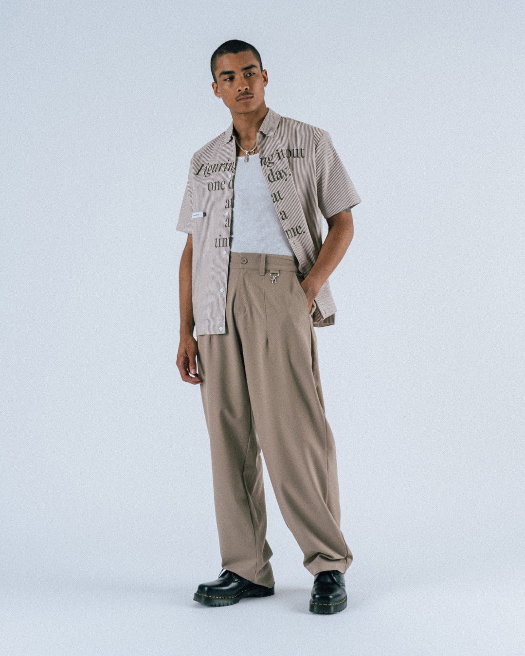 Man wearing a beige shirt with text pattern and beige pants on a white background
