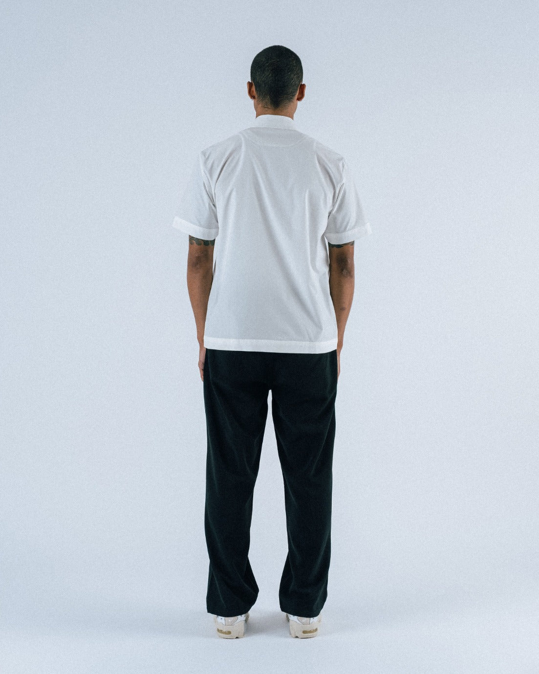 Person wearing a white t-shirt and black pants standing against a light gray background