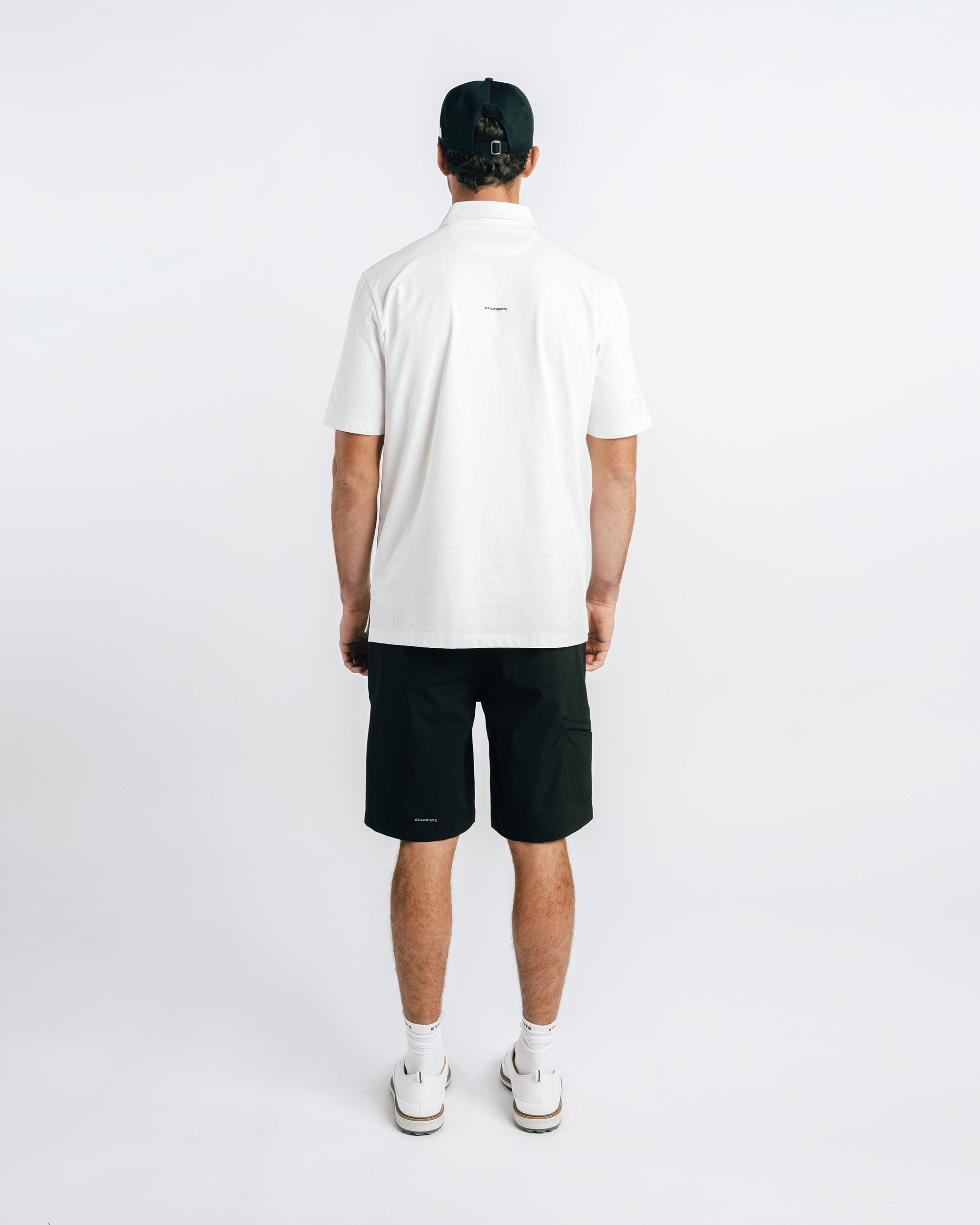 Person wearing a white polo shirt and black shorts on a plain background