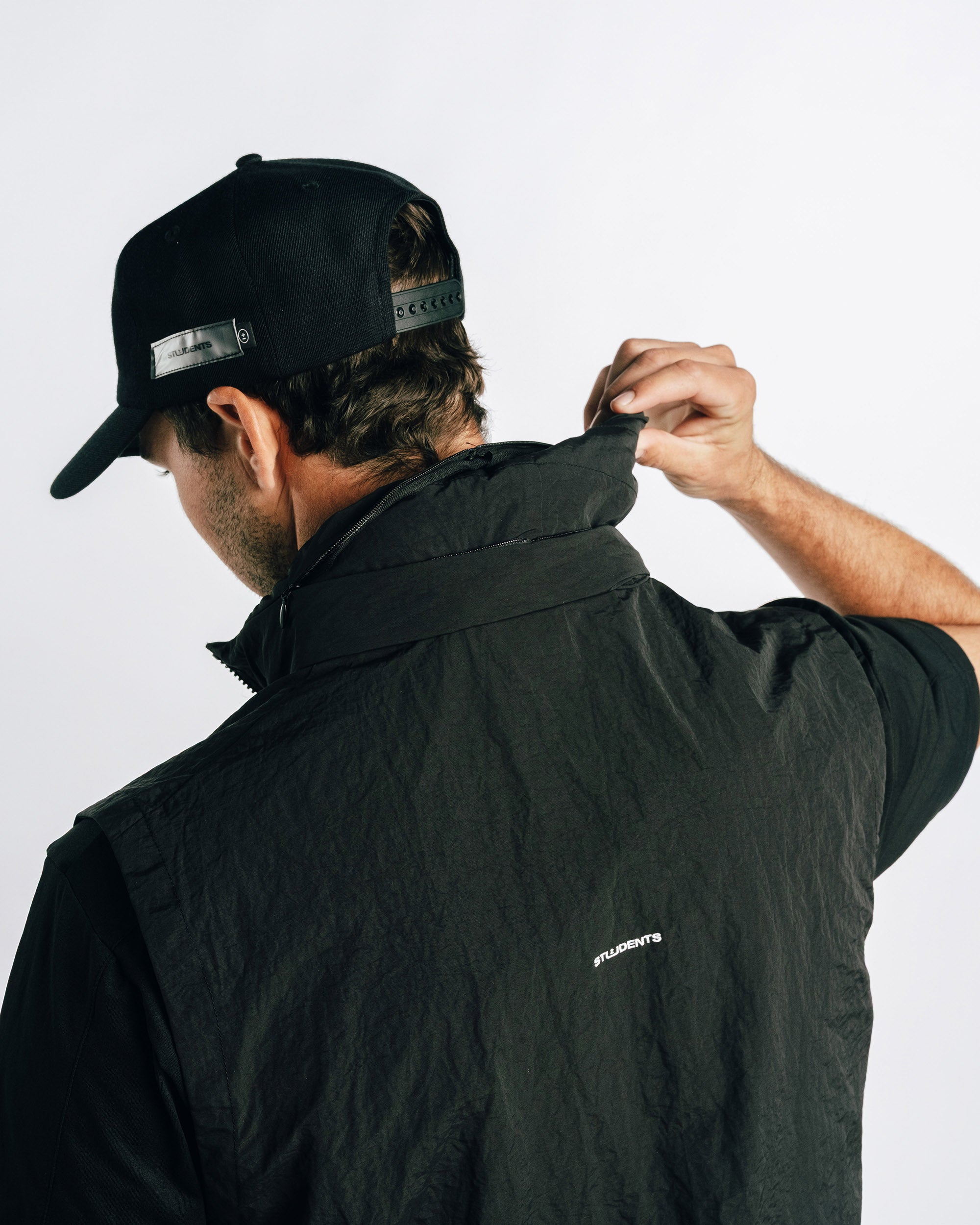 Person wearing a black jacket and cap with visible branding on a white background