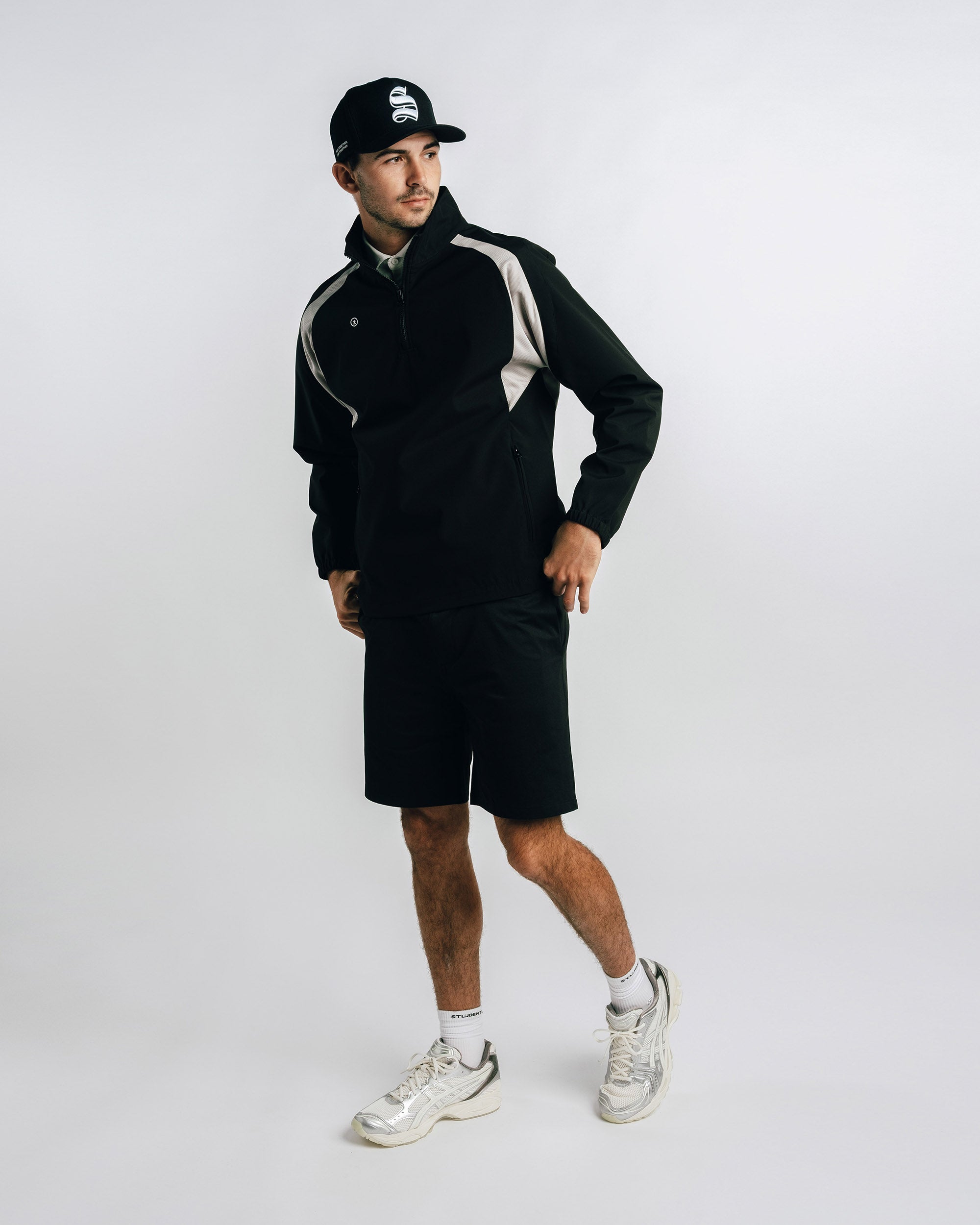 Person wearing a black outfit with white sneakers on a plain background