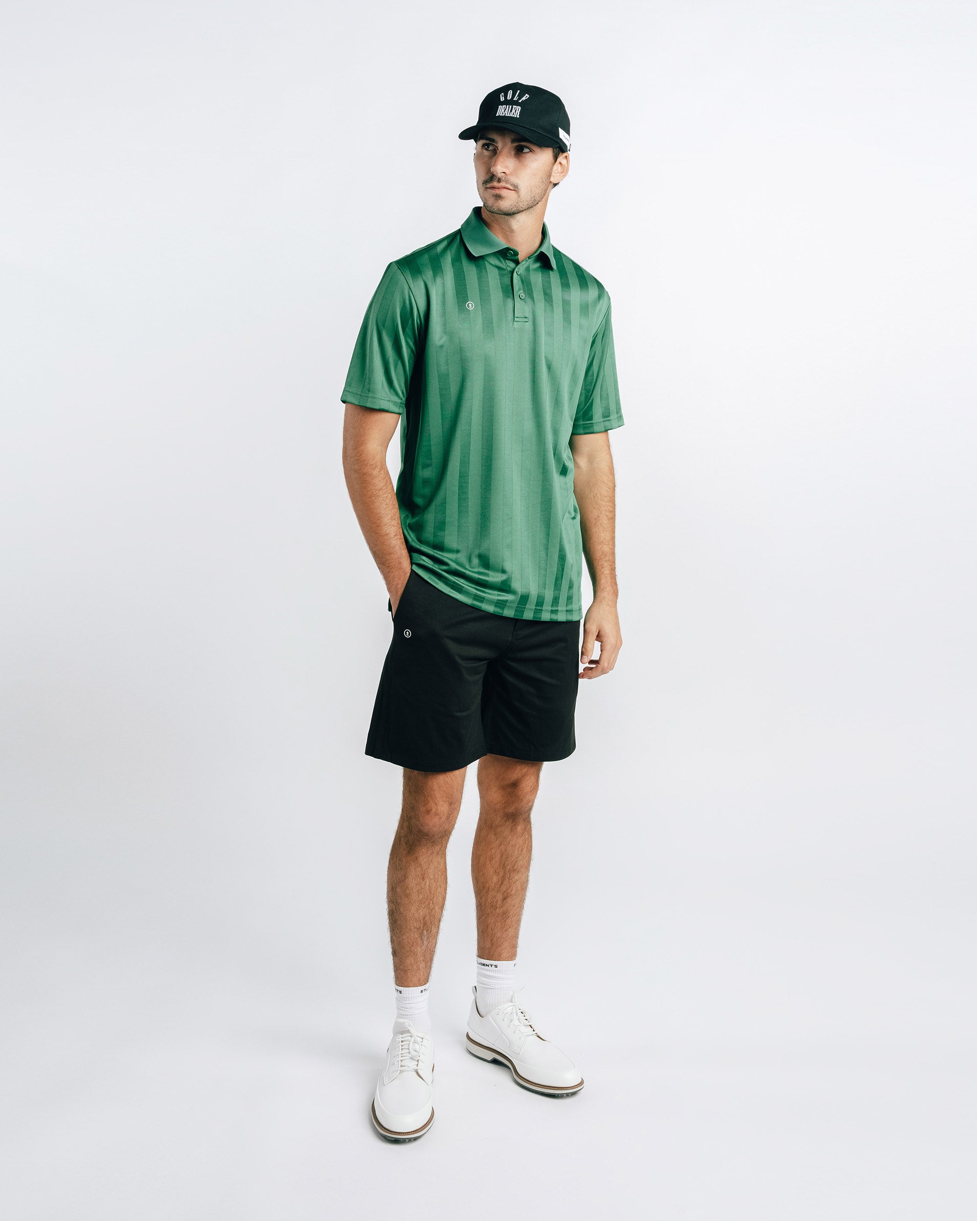 Man wearing a green polo shirt, black shorts, and white shoes on a white background