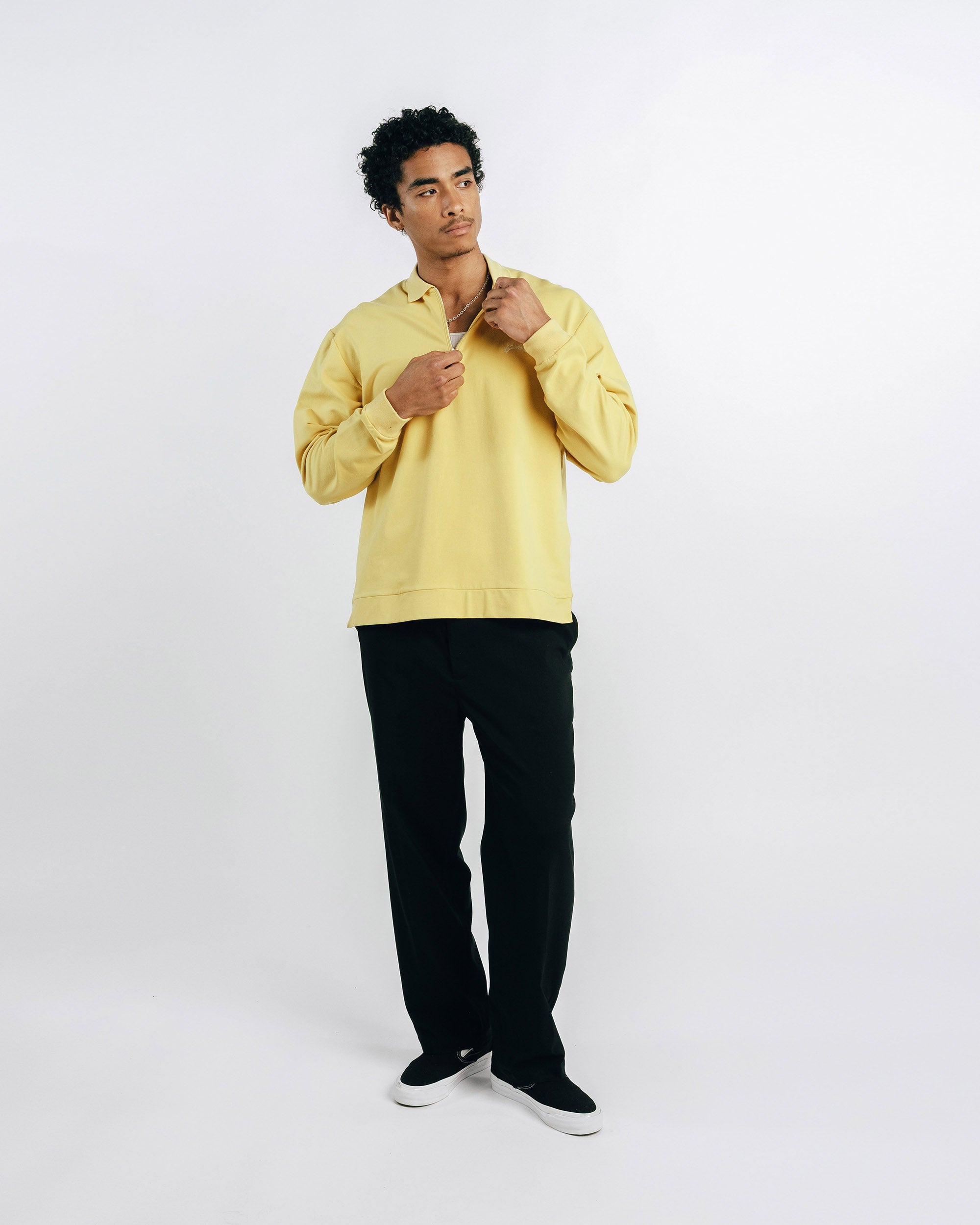 Man wearing a yellow sweater and black pants on a white background