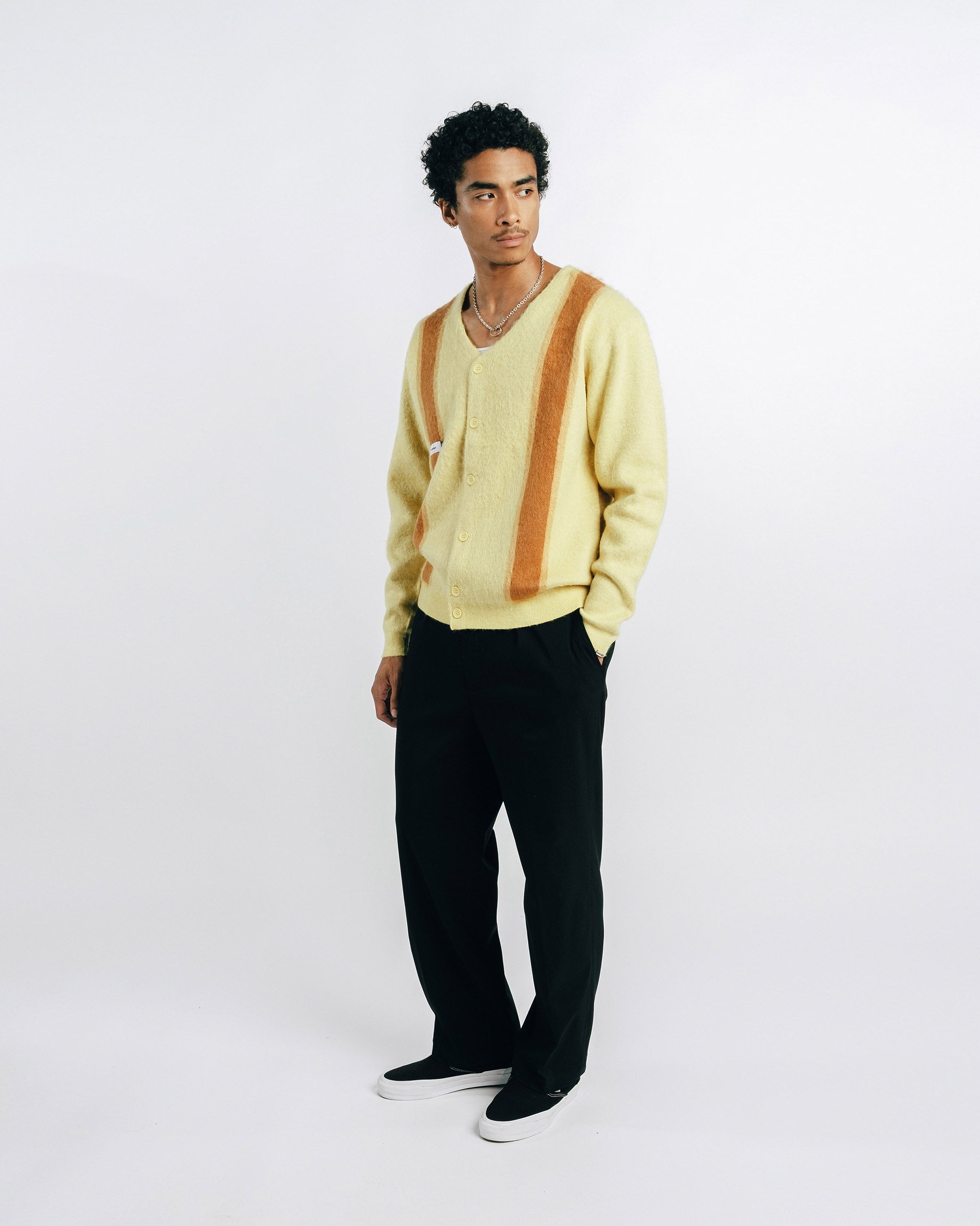 Man wearing a light yellow cardigan with brown stripes on a white background