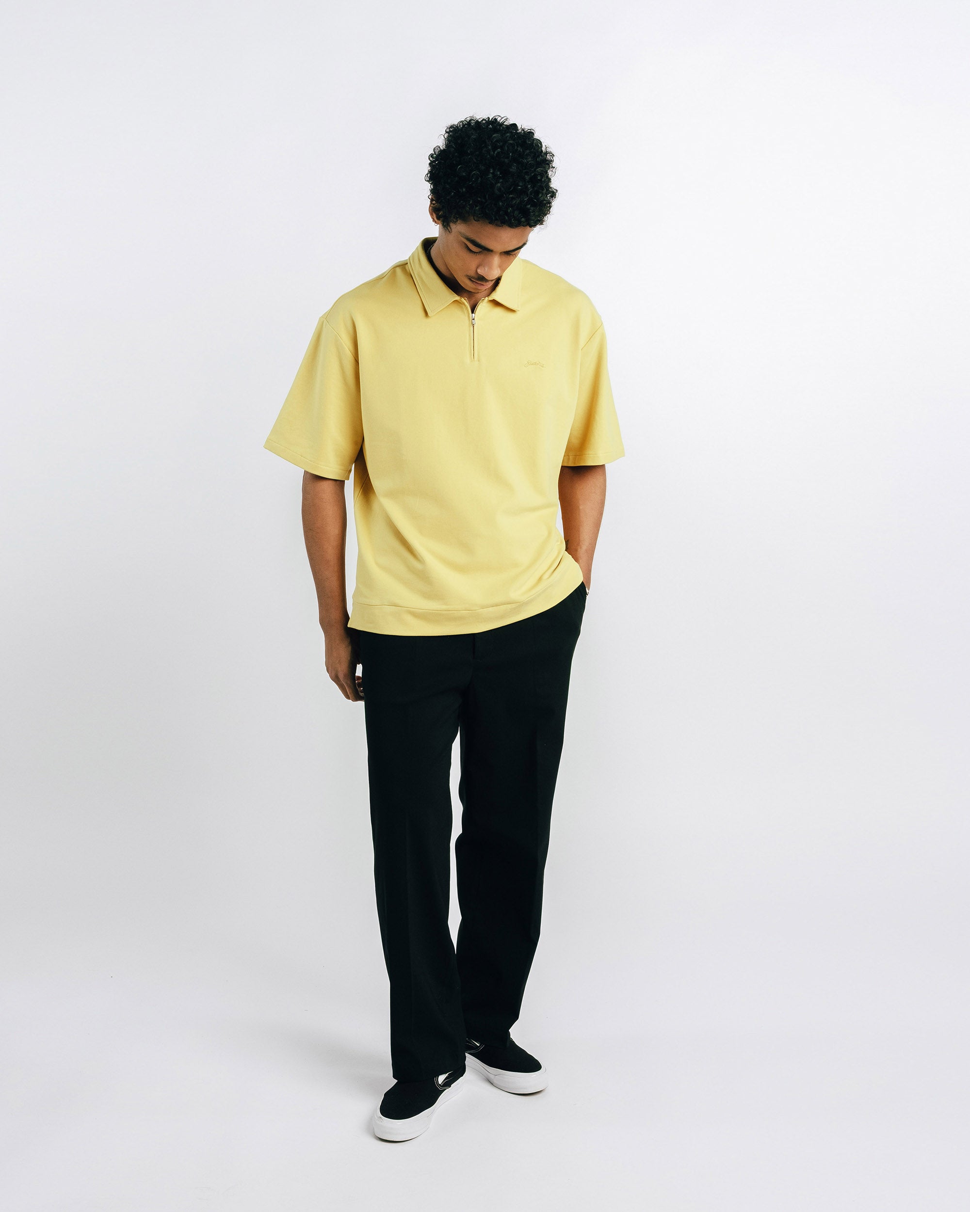 Person wearing a yellow polo shirt and black pants on a white background