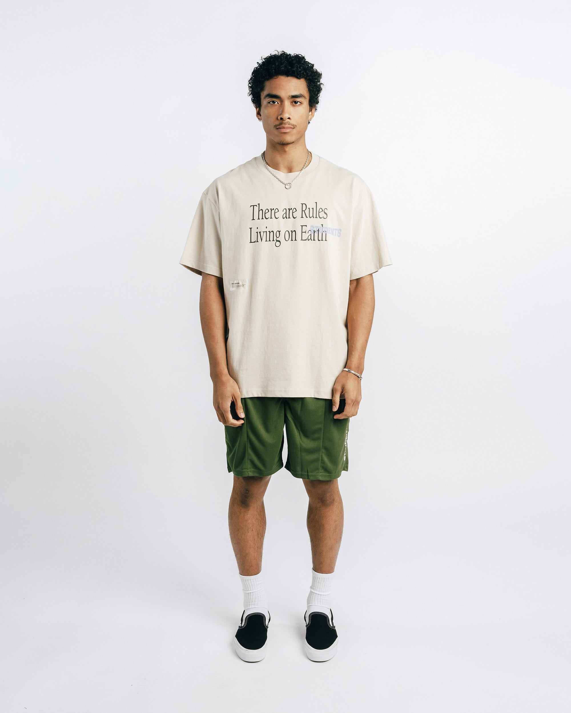 Person wearing a beige t-shirt with text and green shorts on a white background