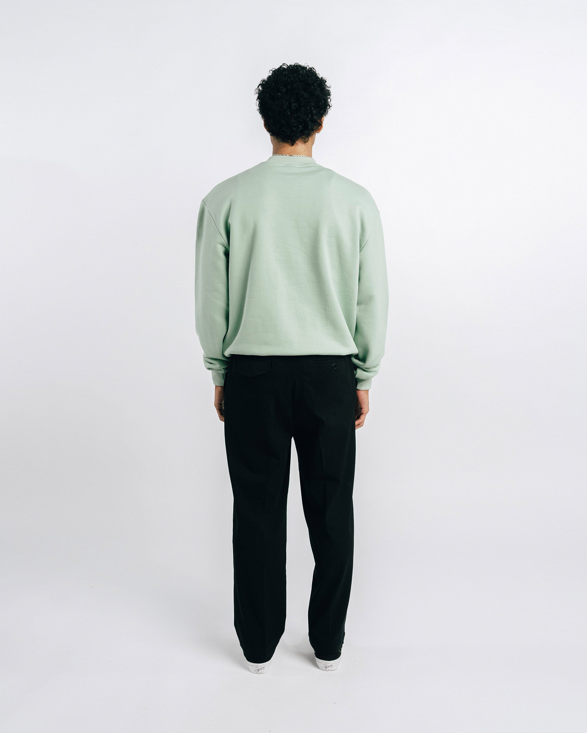 Person wearing a light green sweatshirt with text and black pants on a white background