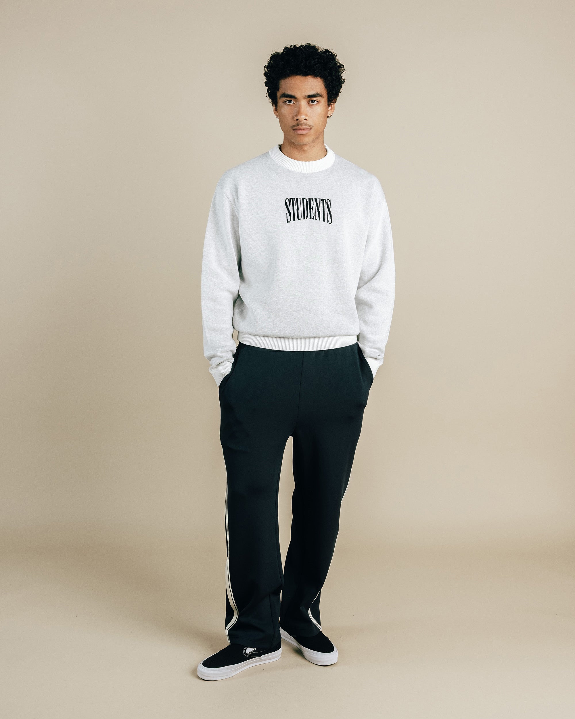Person wearing a white sweatshirt with 'STUDENTS' text and black pants on a beige background