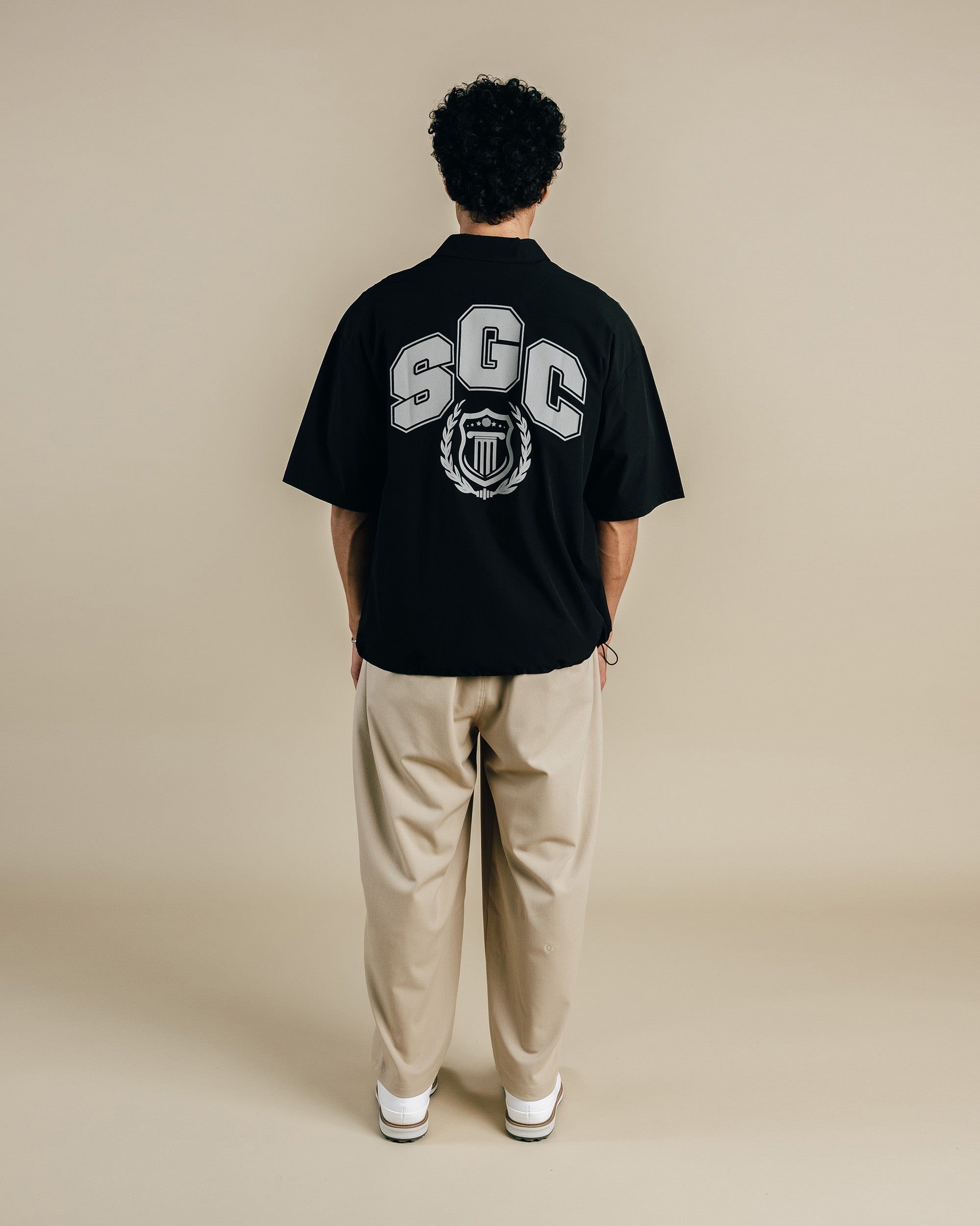 Person wearing a black t-shirt with 'SGC' logo on the back, standing against a beige background