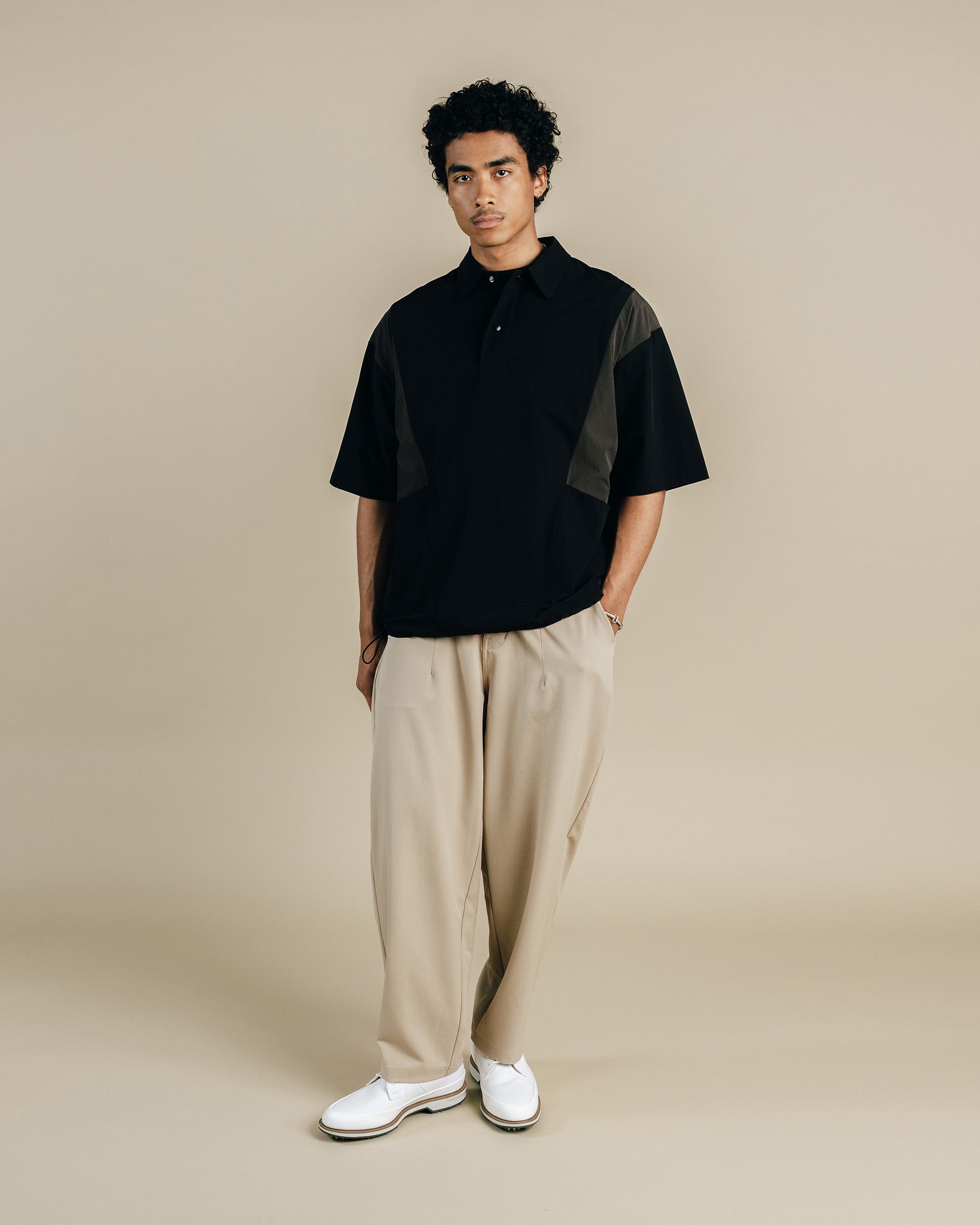 Man wearing a black and grey shirt with beige pants on a beige background