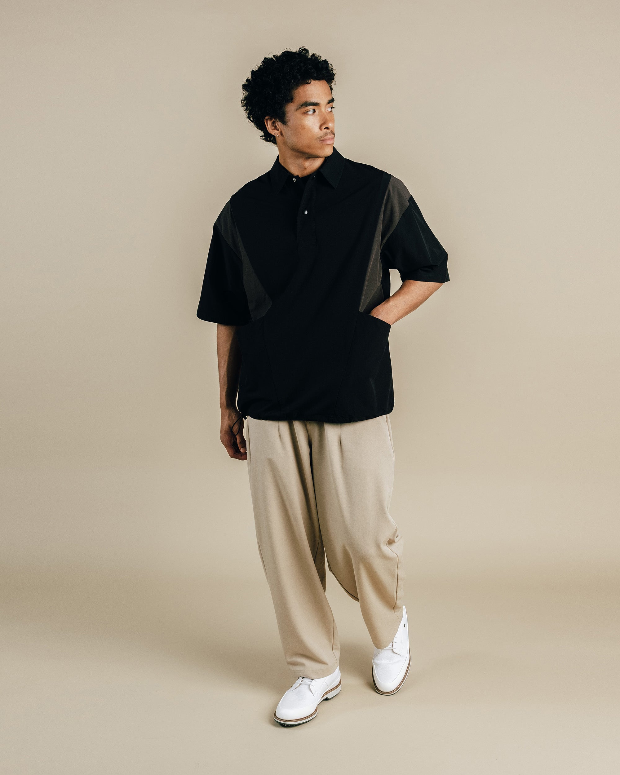 Man wearing a black shirt with a geometric pattern and beige pants on a beige background