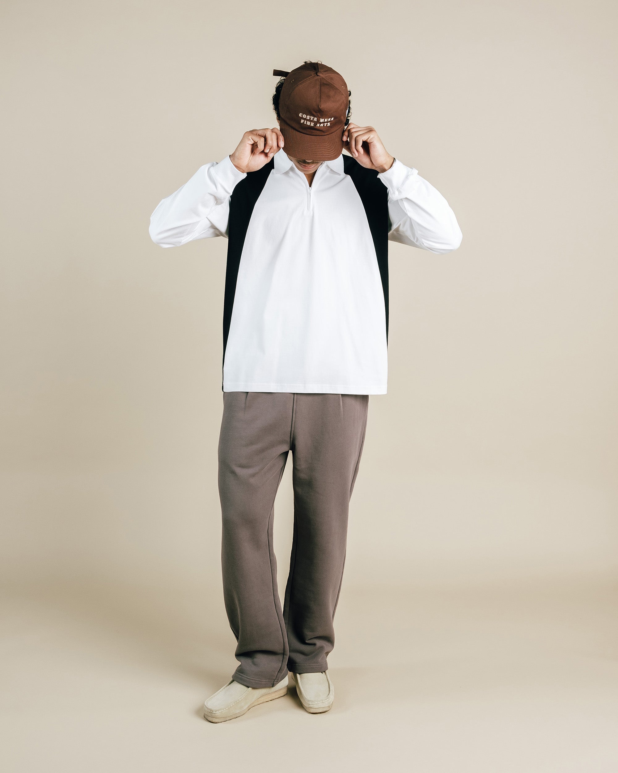 Person wearing a white shirt, gray pants, and beige shoes on a beige background