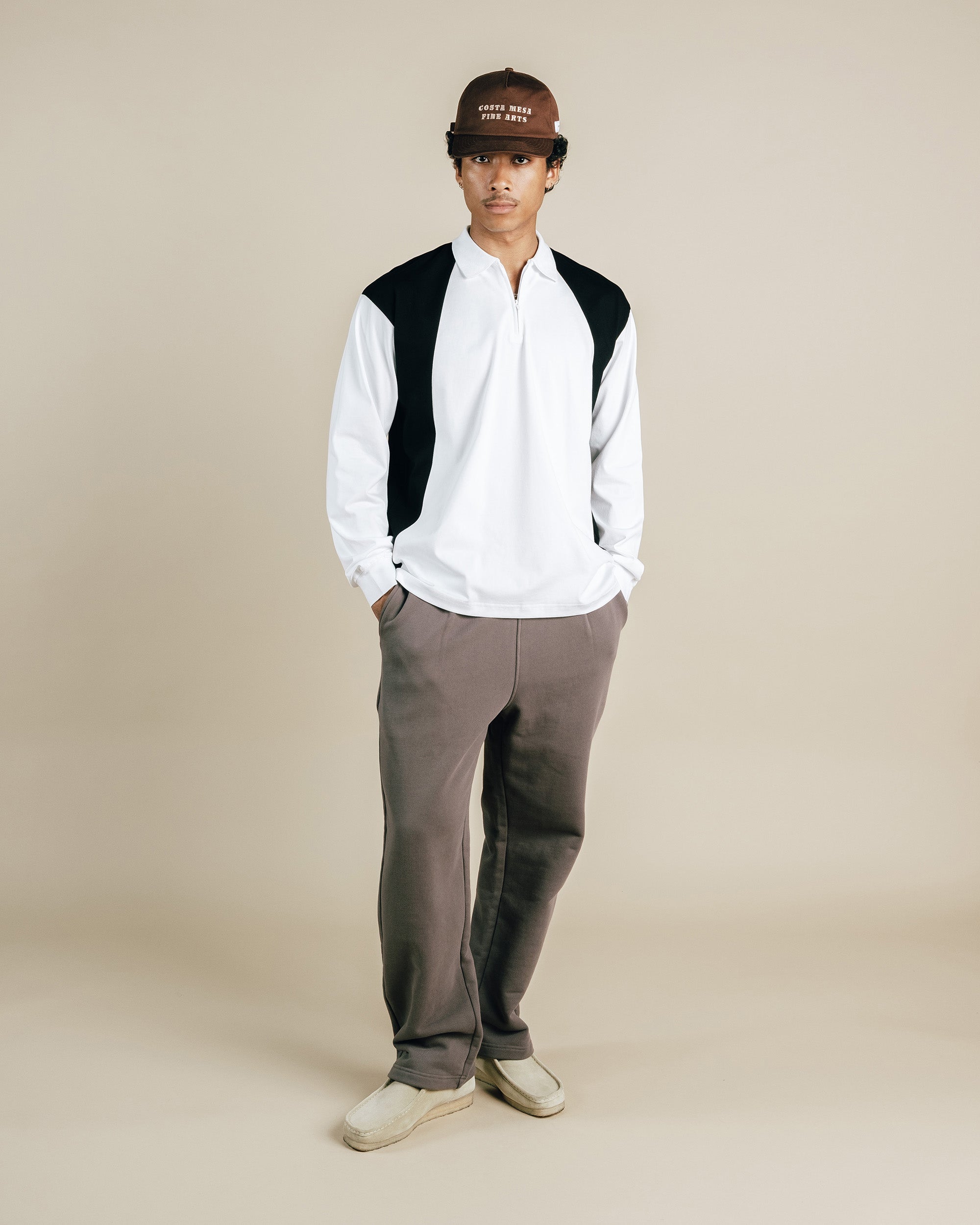 Person wearing a white shirt, brown pants, and a cap on a beige background