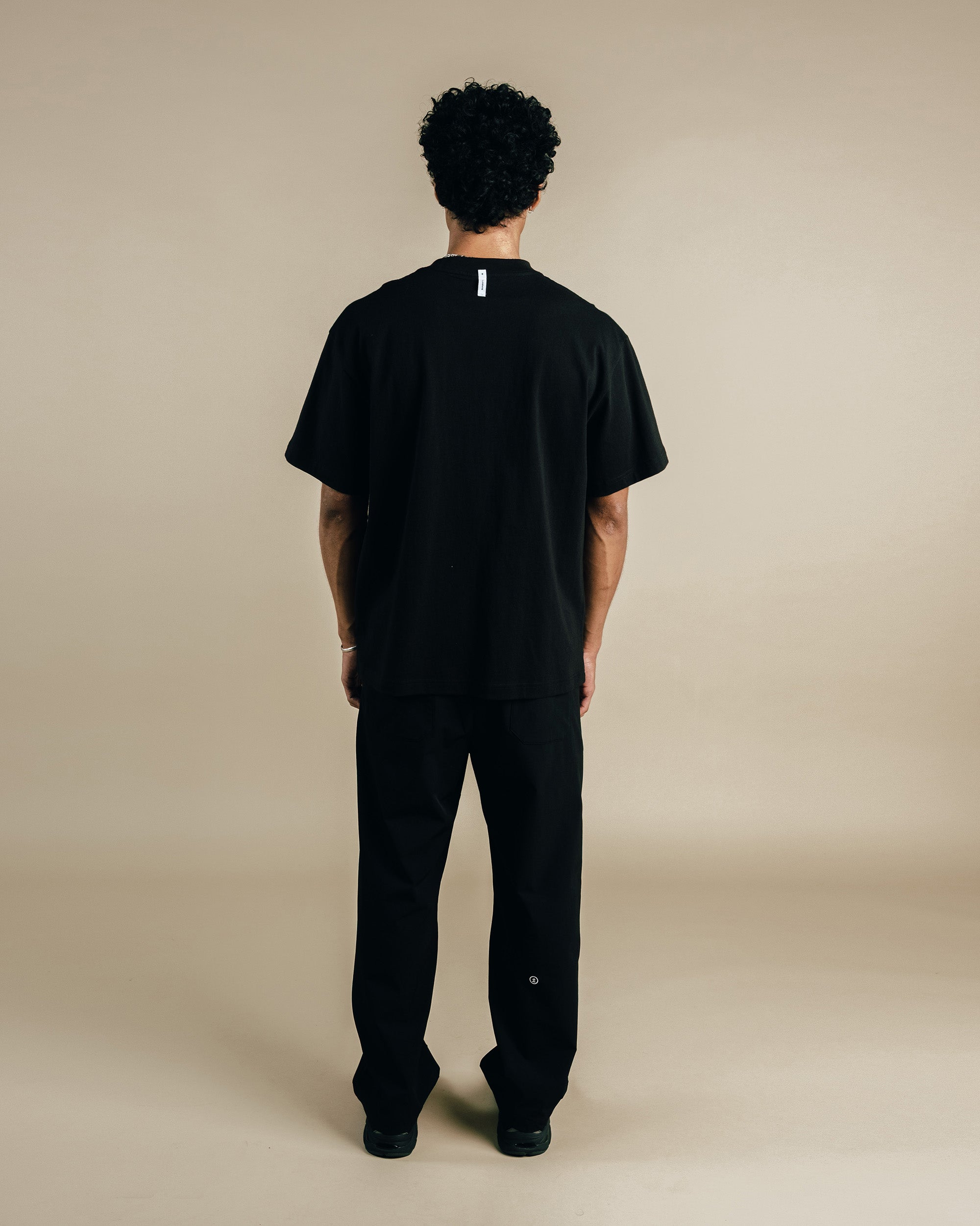 Person wearing a black t-shirt and pants on a beige background