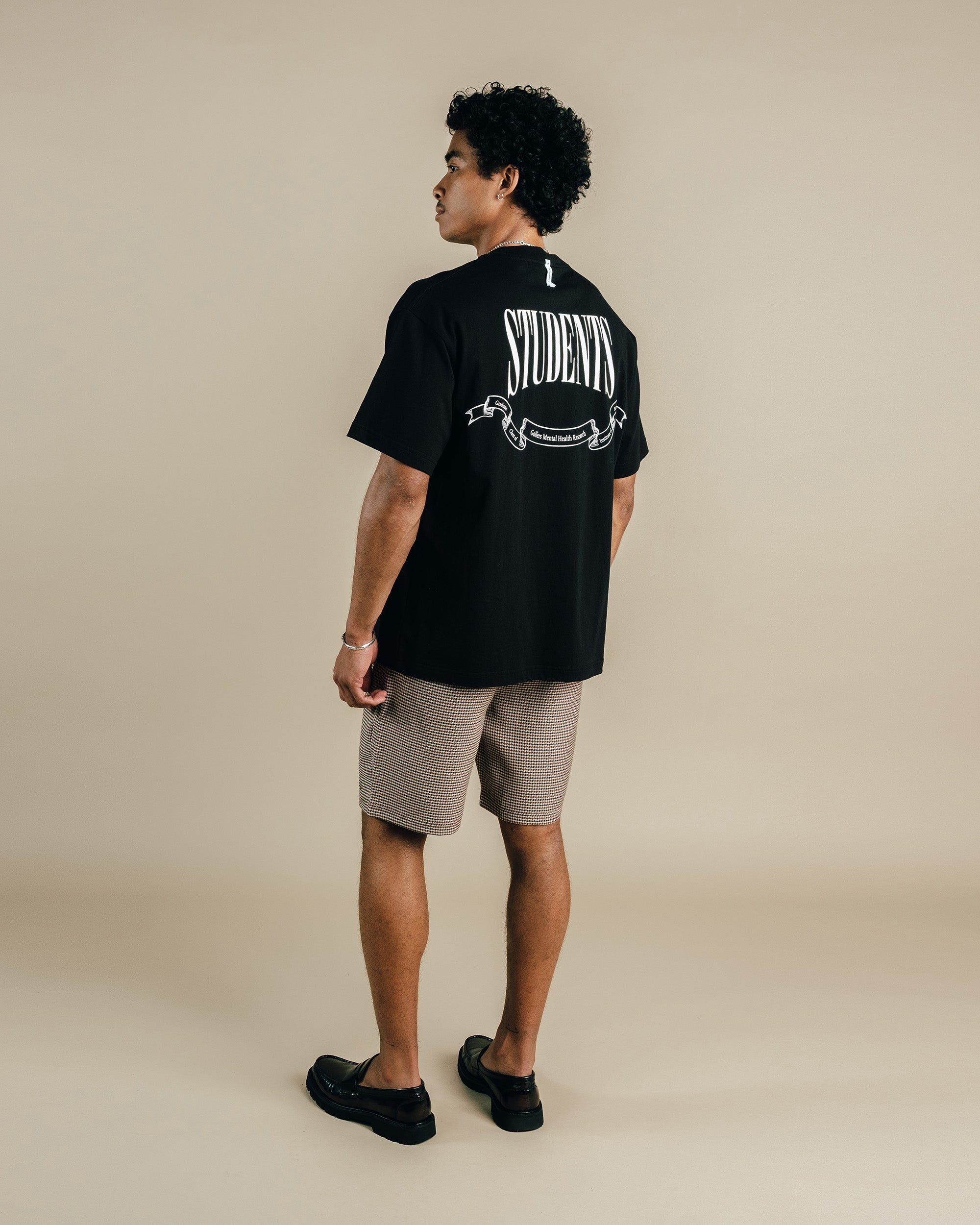 Person wearing a black t-shirt with 'STUDENTS' printed on the back, standing against a beige background.