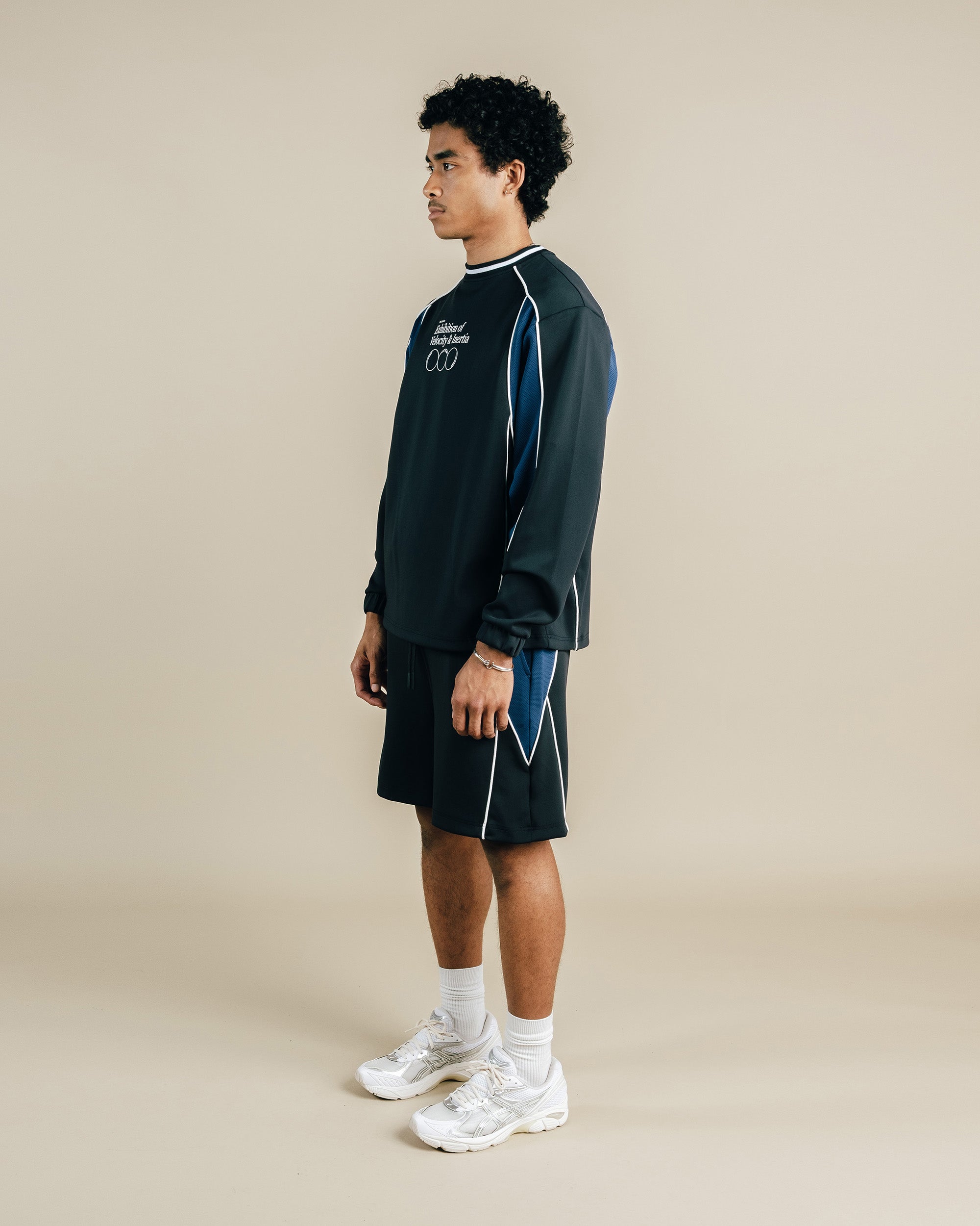 Person wearing a dark athletic outfit with white sneakers on a beige background