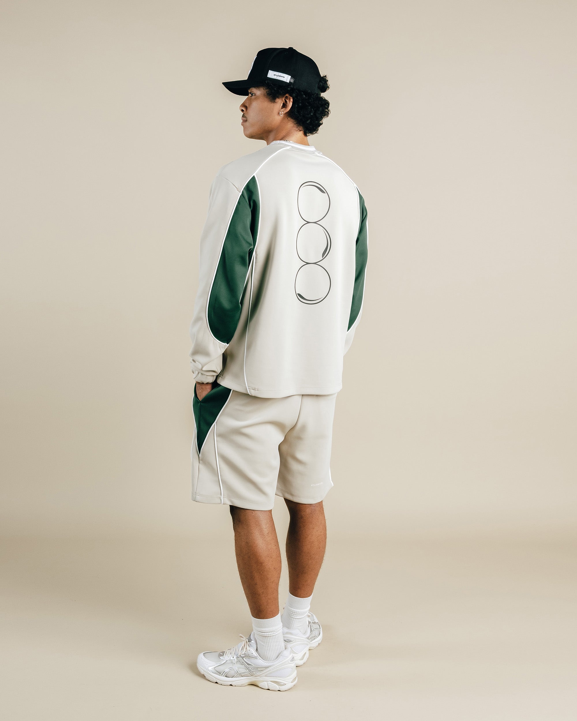 Person wearing a white and green outfit with a cap on a beige background