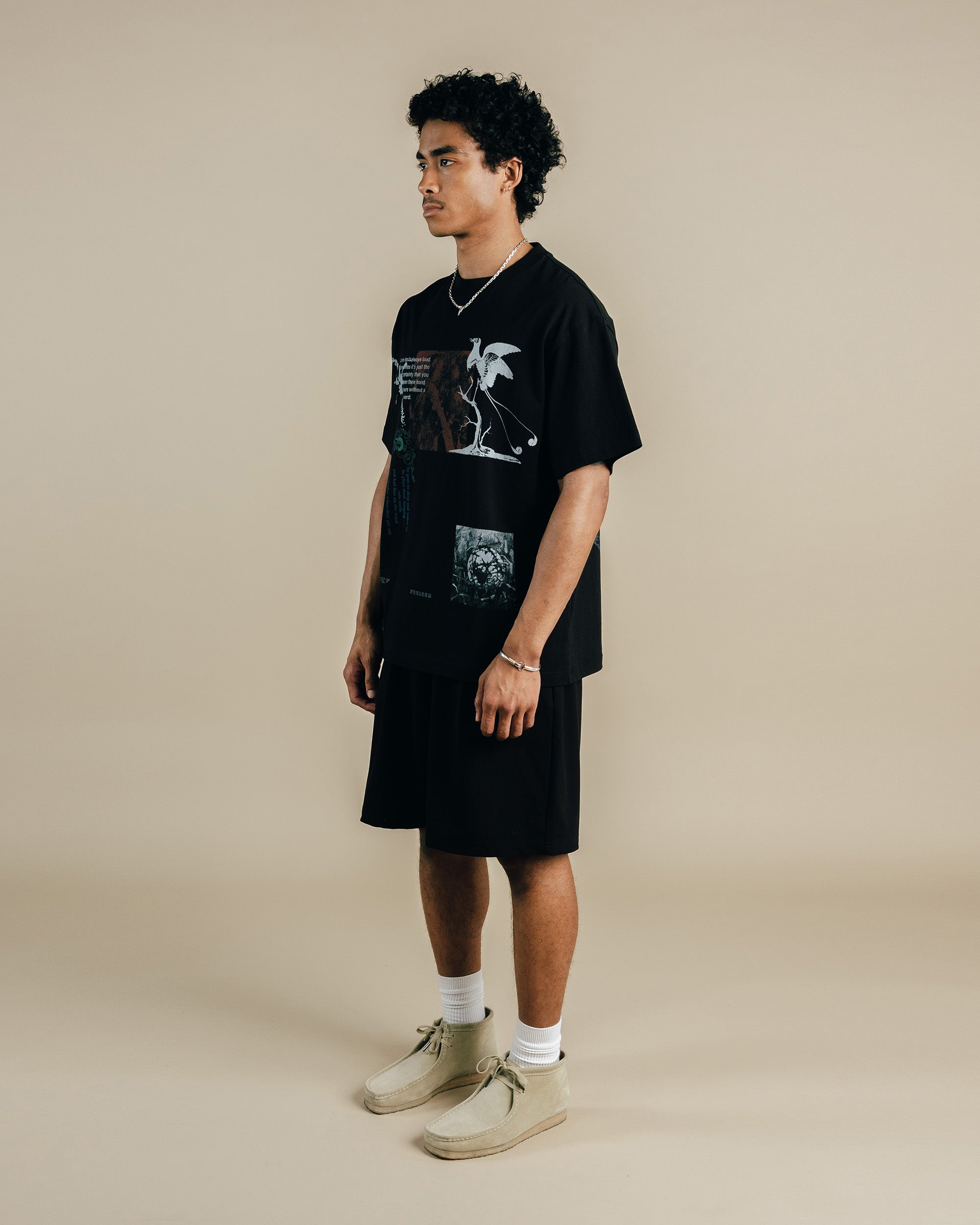 Person wearing a black graphic t-shirt and shorts on a beige background