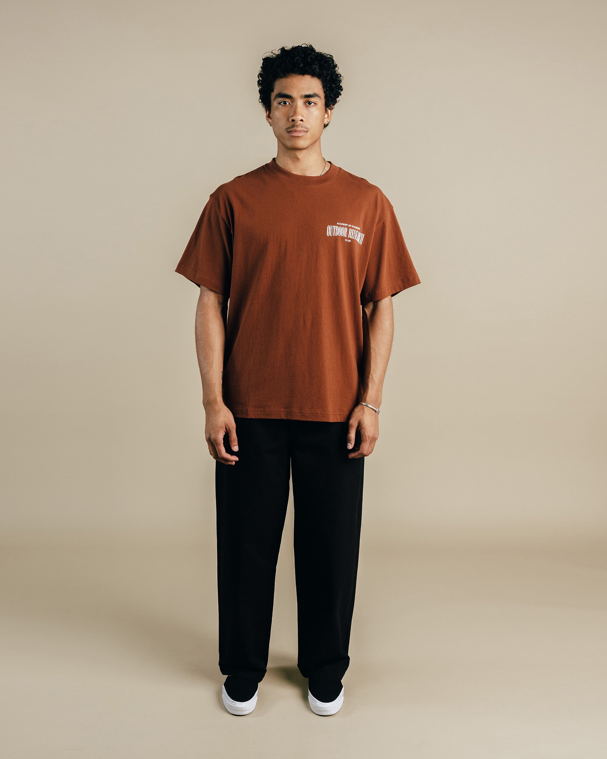 Person wearing a brown t-shirt and black pants on a beige background