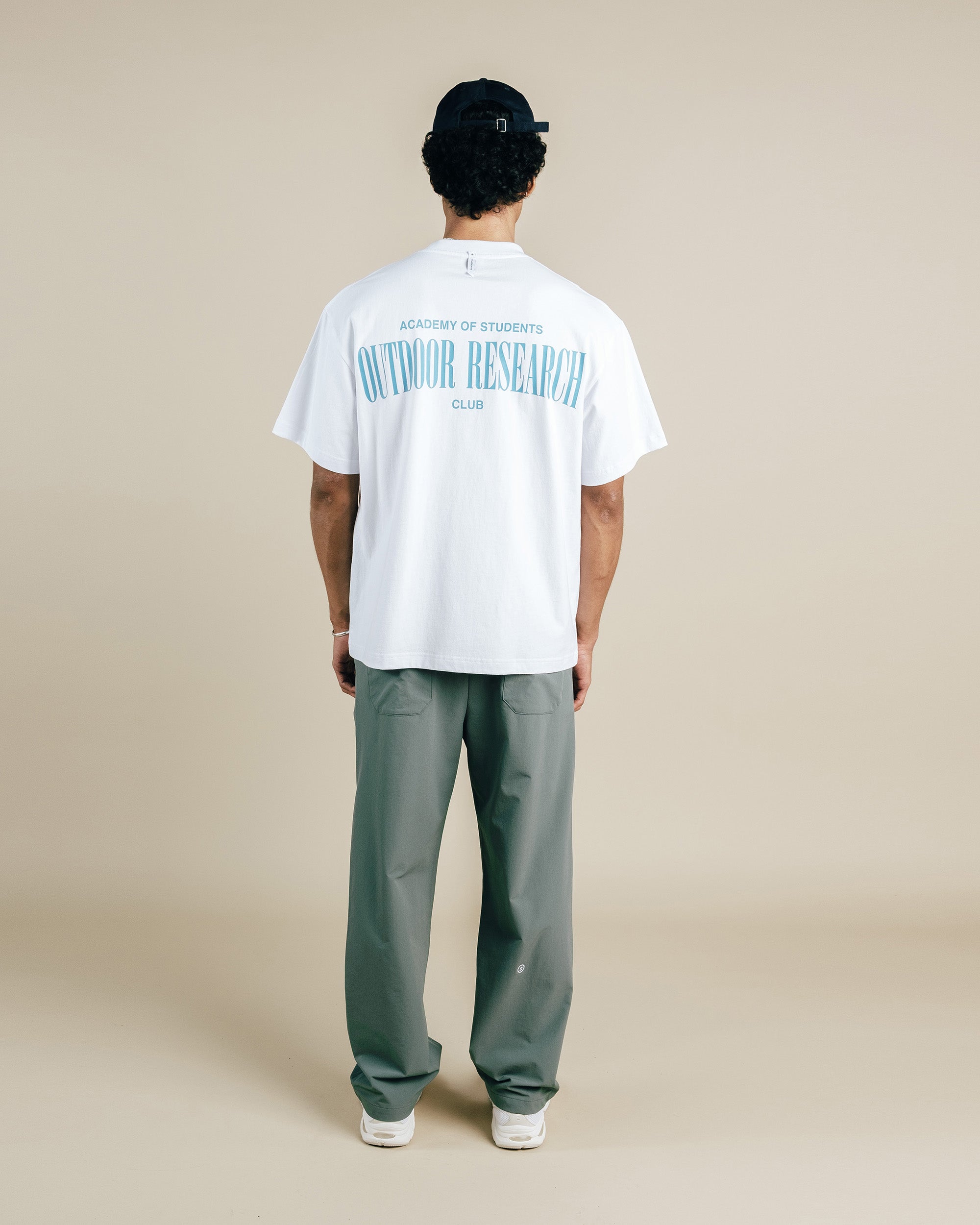 Person wearing a white t-shirt with text and gray pants on a beige background