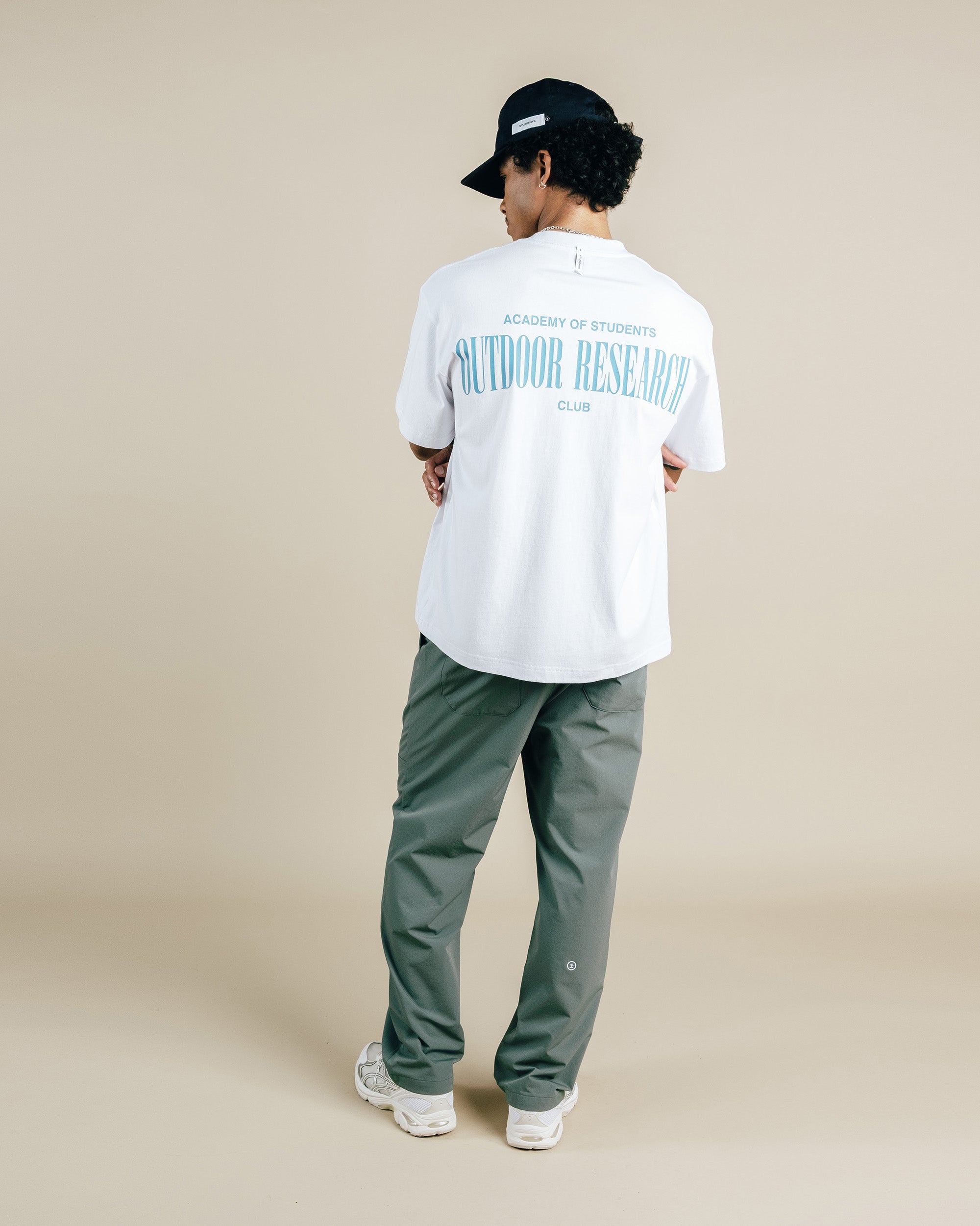 Person wearing a white t-shirt with text and green pants on a beige background