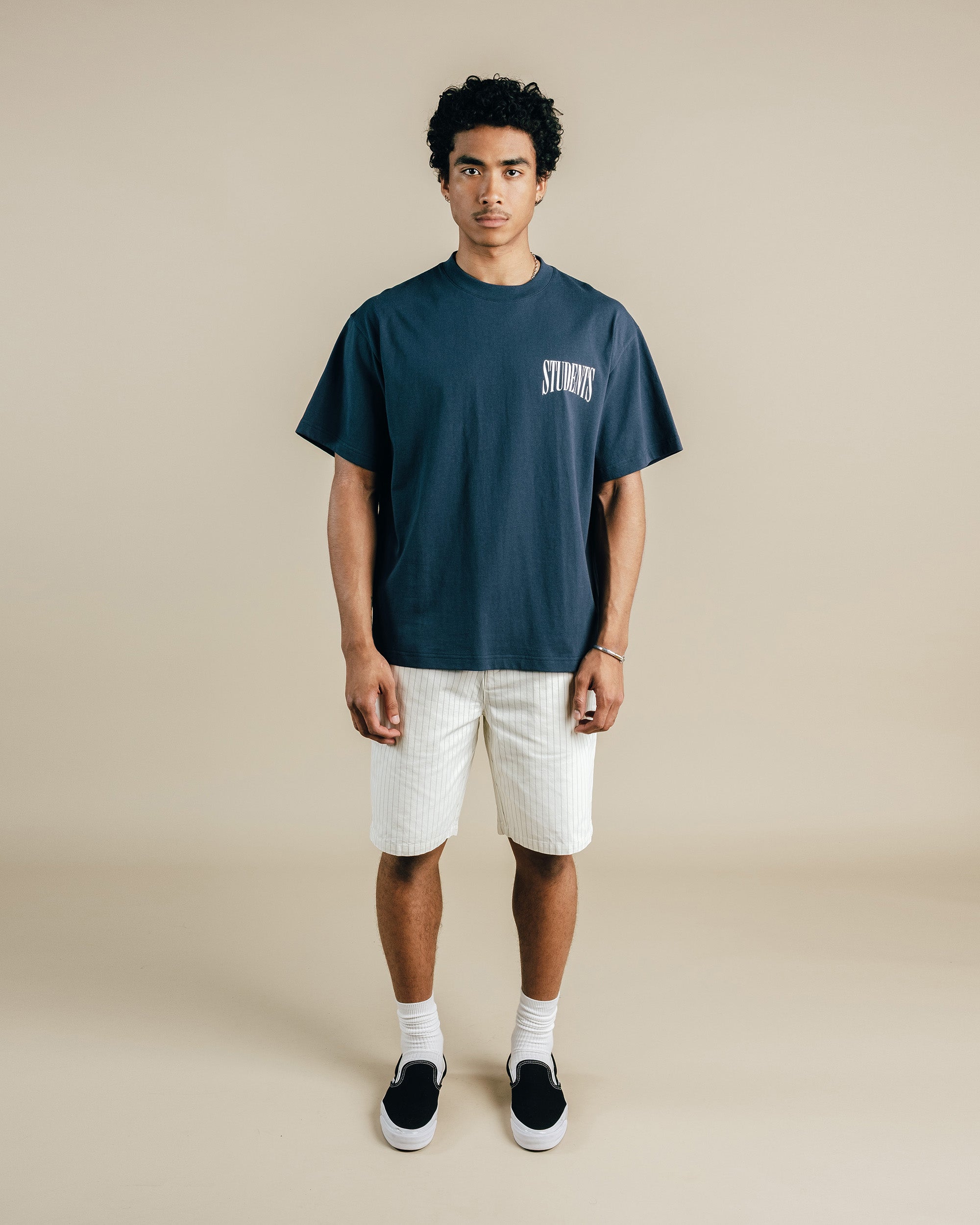 Person wearing a navy t-shirt with text and white shorts on a beige background
