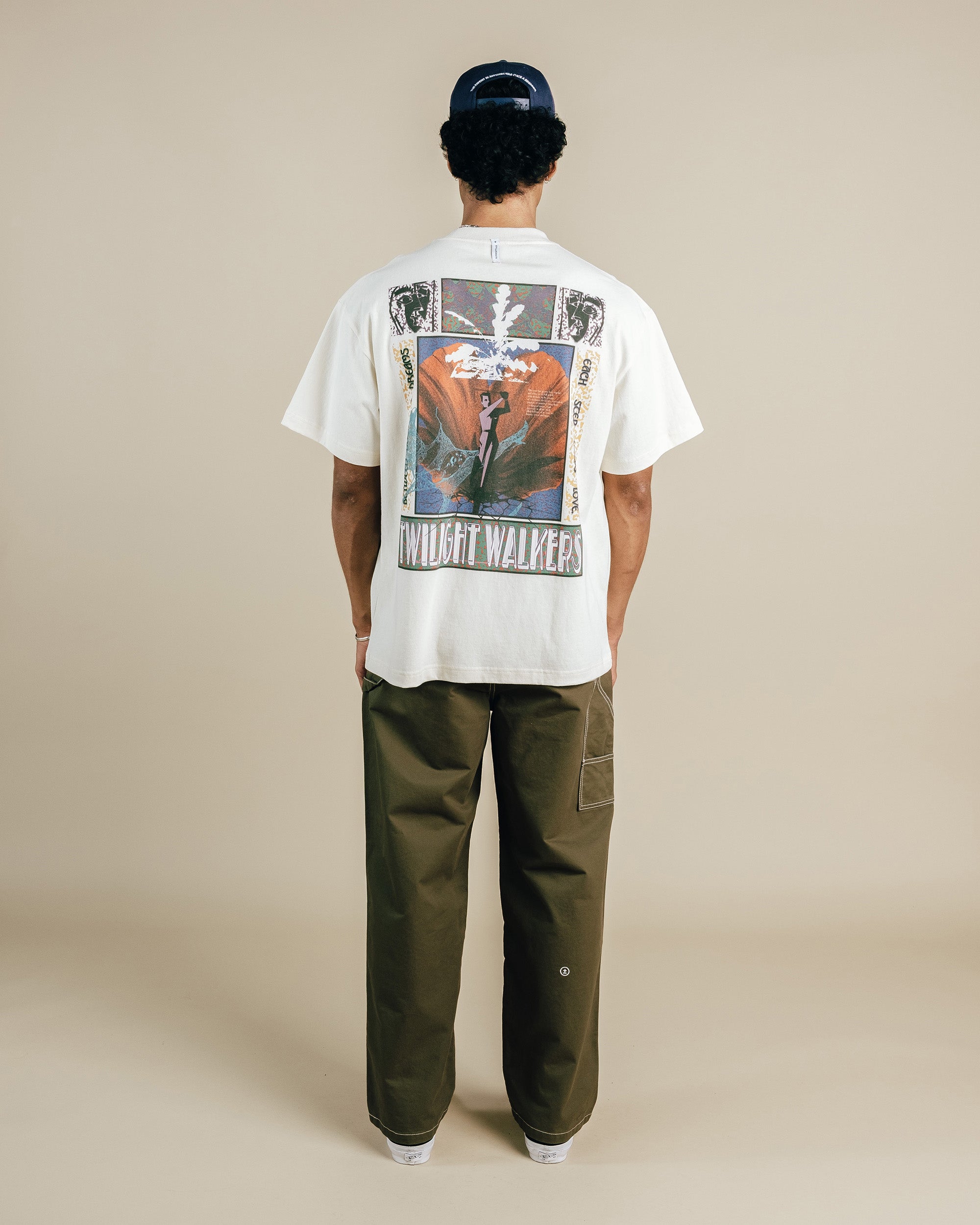 Person wearing a nude t-shirt with a graphic design on the back, standing against a beige background
