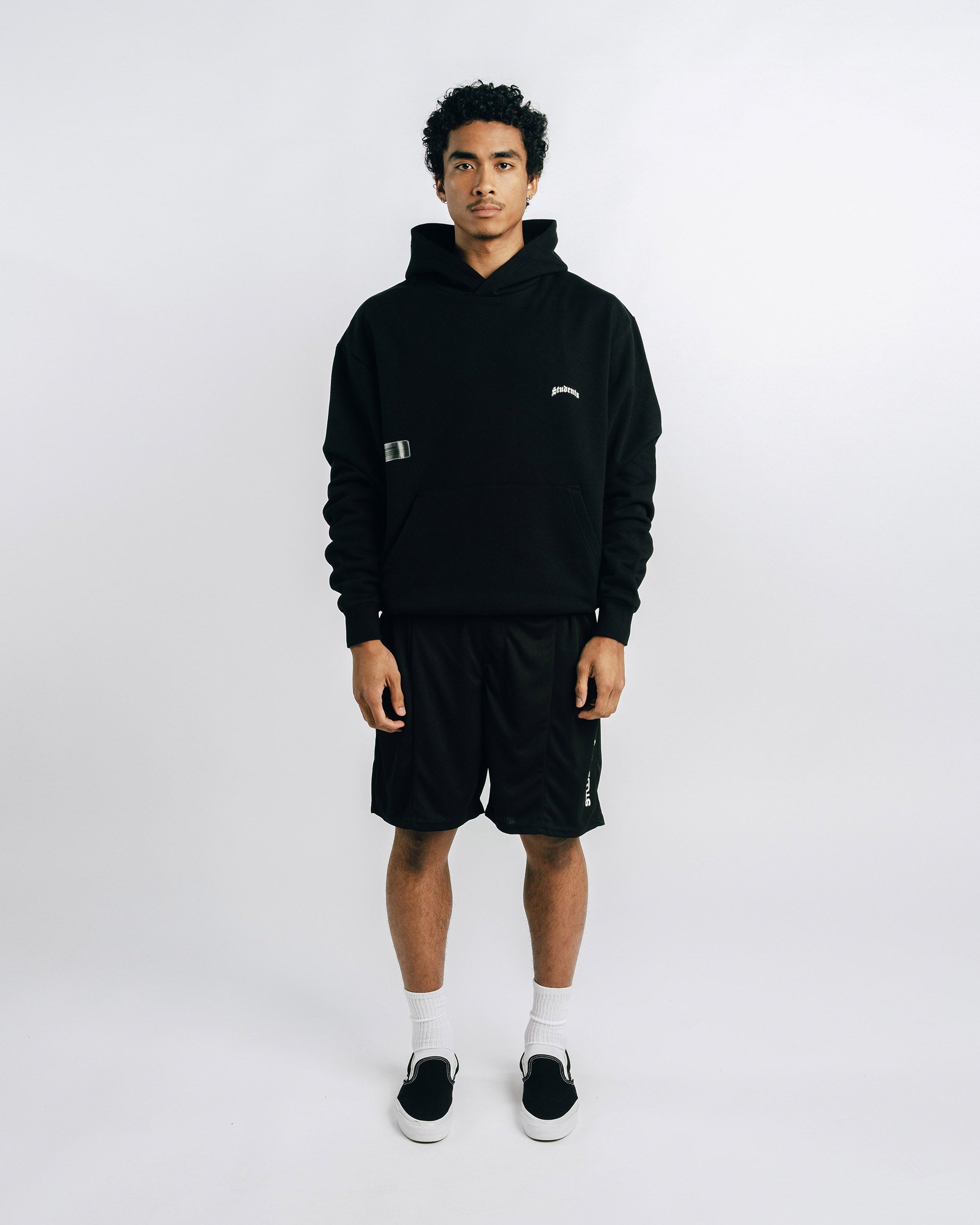 Person wearing a black hoodie and shorts set on a white background