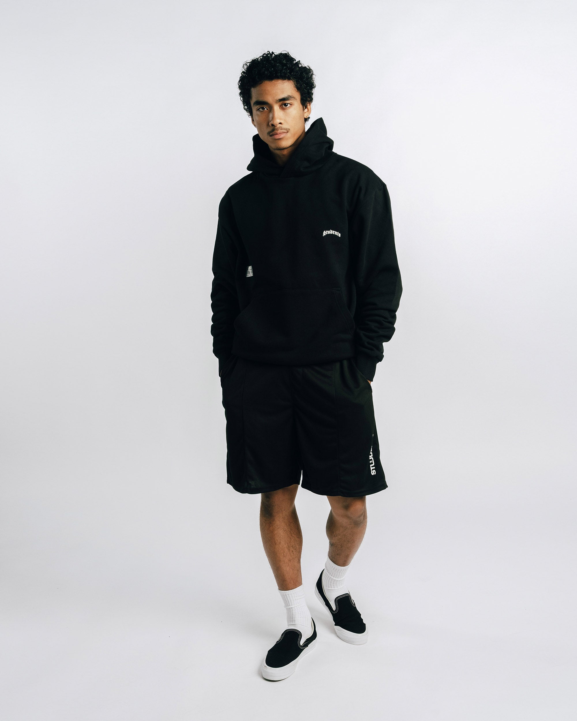 Person wearing a black hoodie and shorts with visible branding on a white background