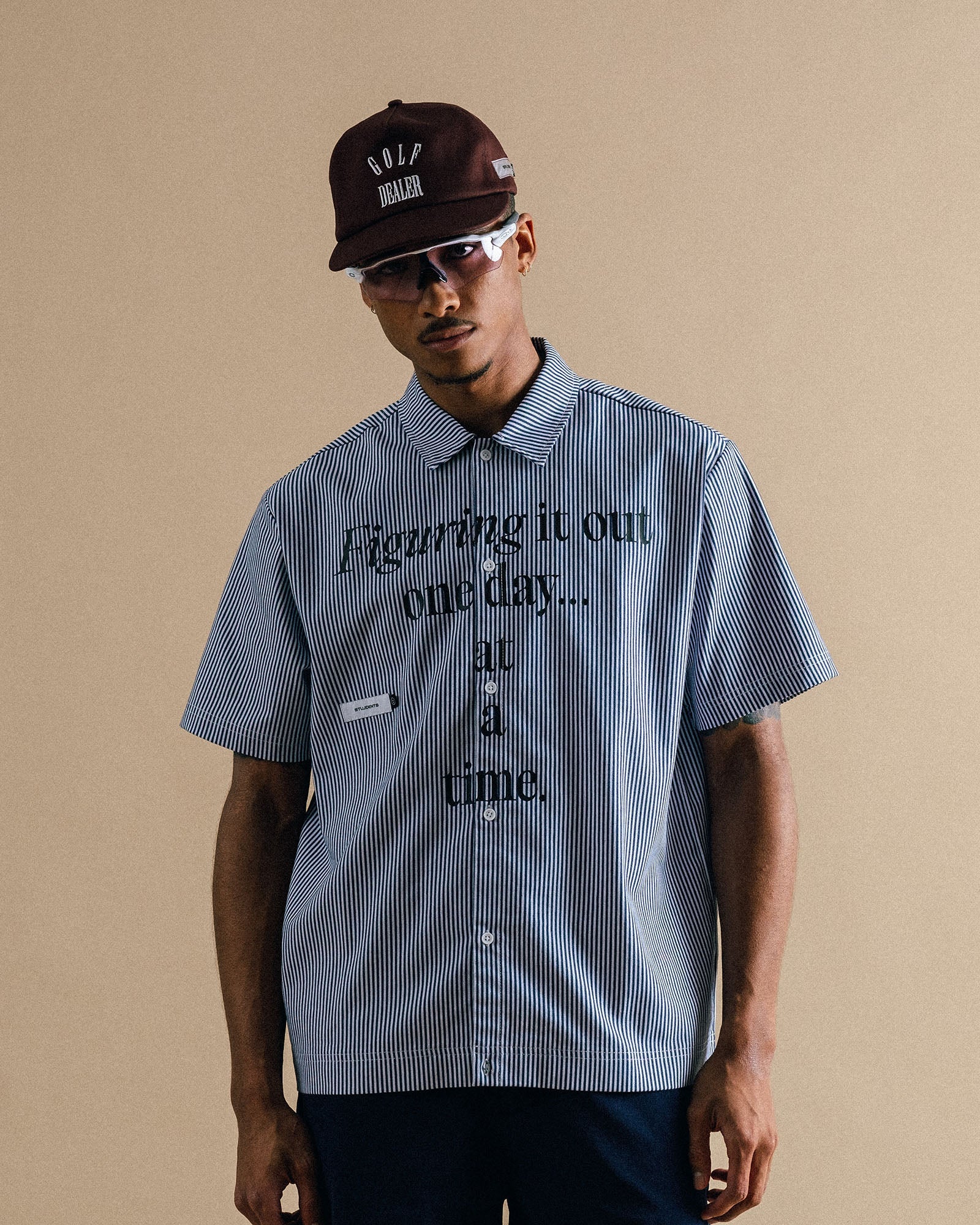 Man wearing a blue shirt with text and a cap on a beige background