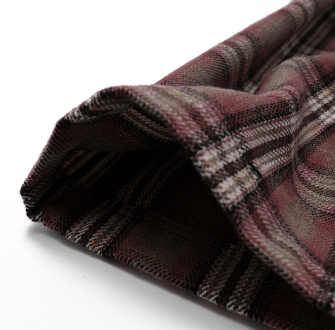 Close-up of a plaid fabric with brown, red, and beige colors on a white background.