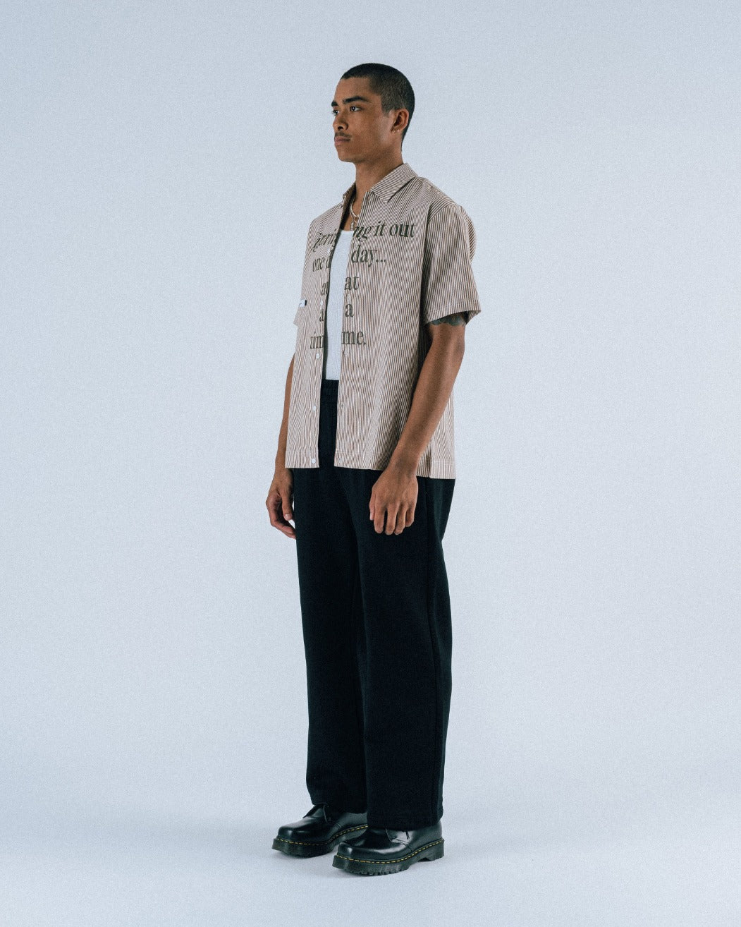 Person wearing a patterned shirt and black pants on a white background
