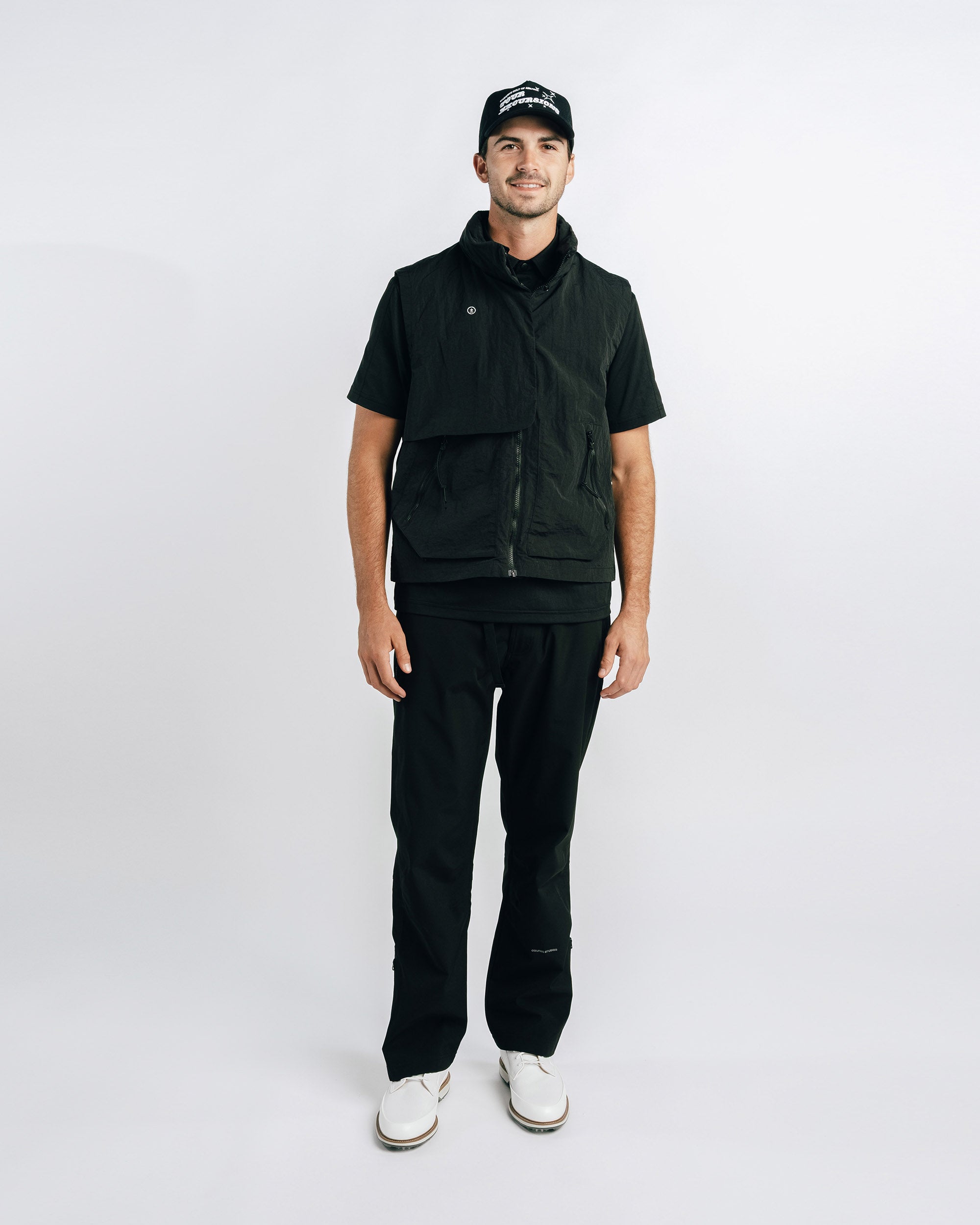 Man wearing a black outfit with a vest and cap on a white background