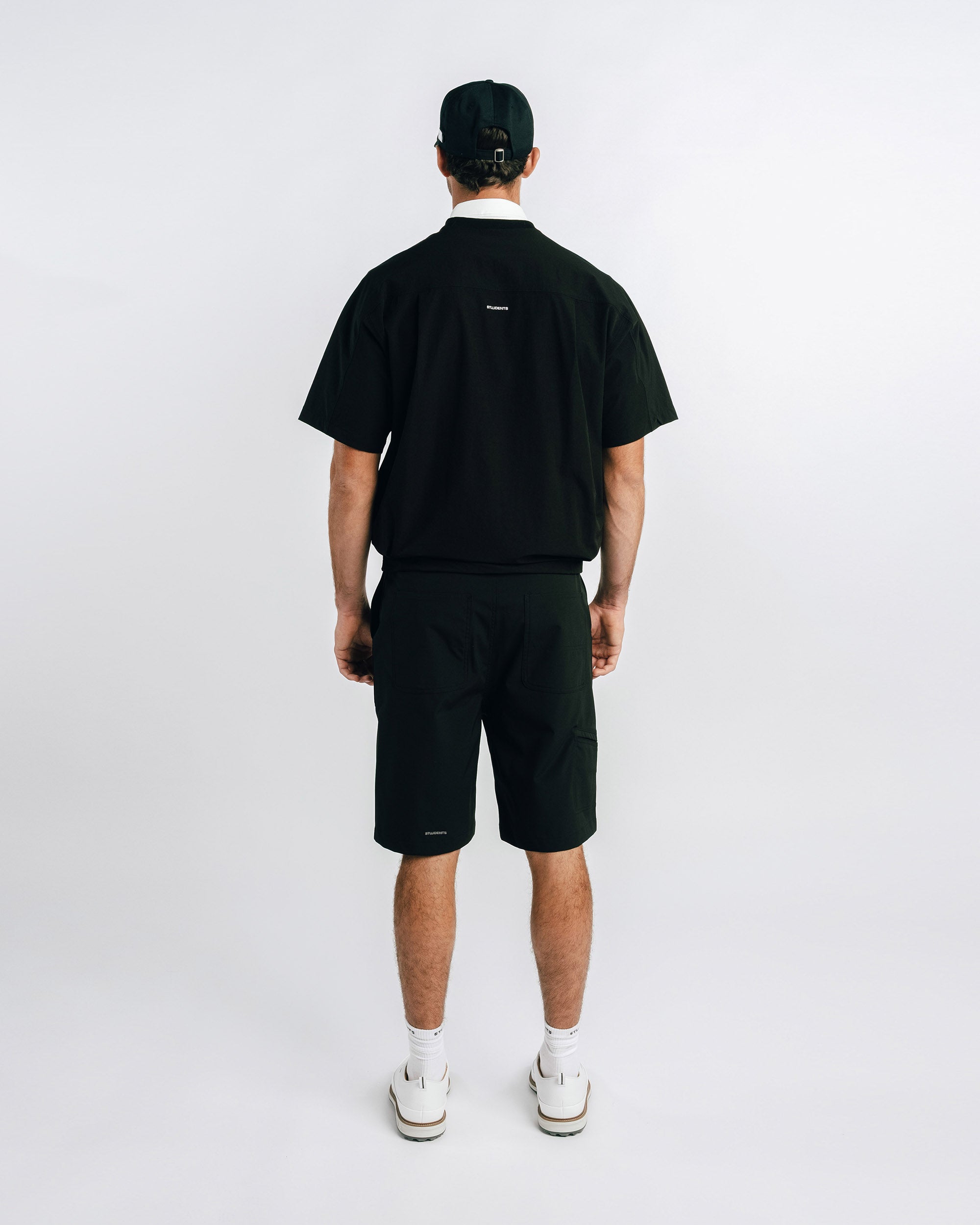 Person wearing a black t-shirt and shorts with a logo on the back, standing against a white background