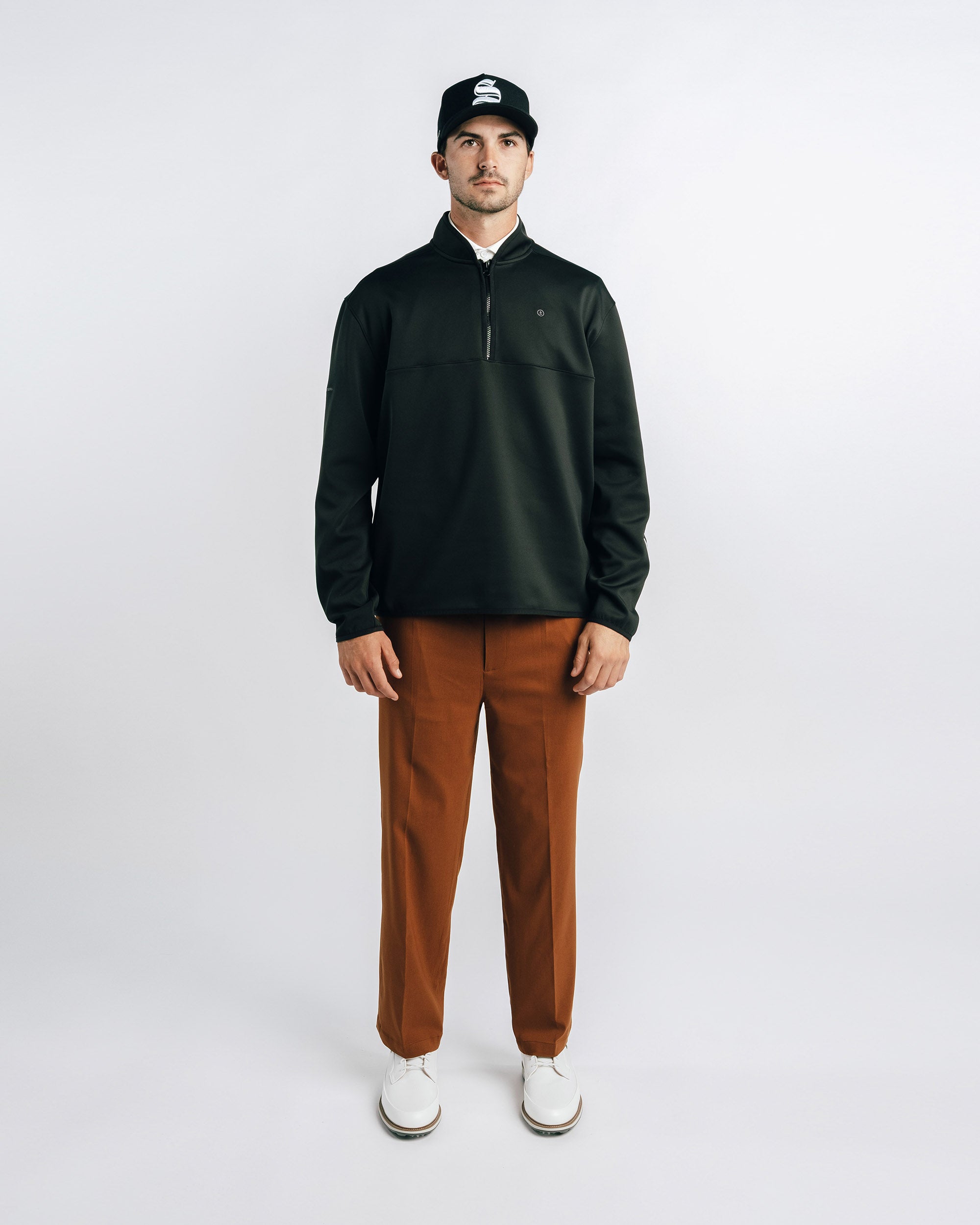 Man wearing a black jacket, brown pants, and a black cap on a white background