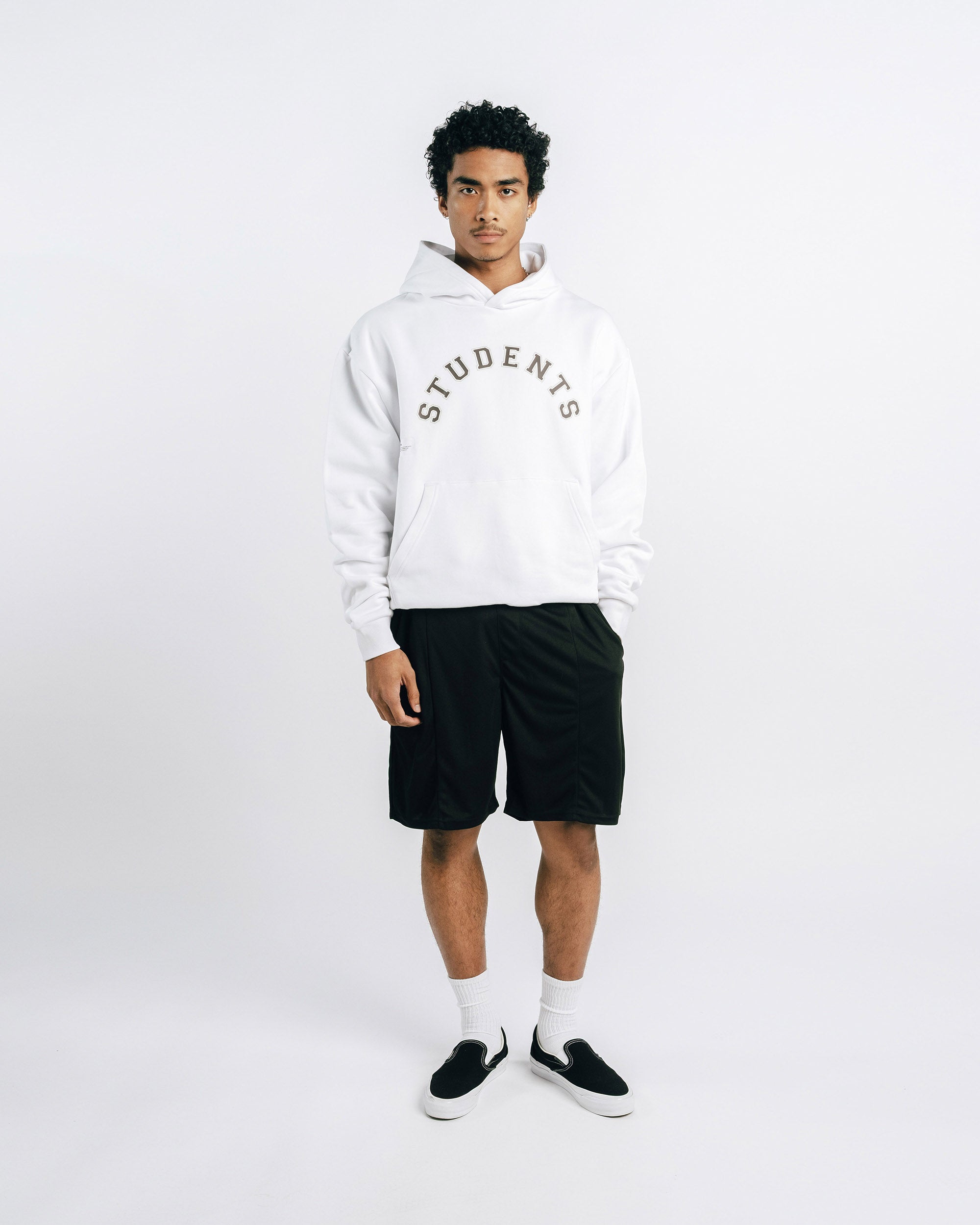 Person wearing a white hoodie with 'STUDENTS' text, black shorts, and black shoes on a white background