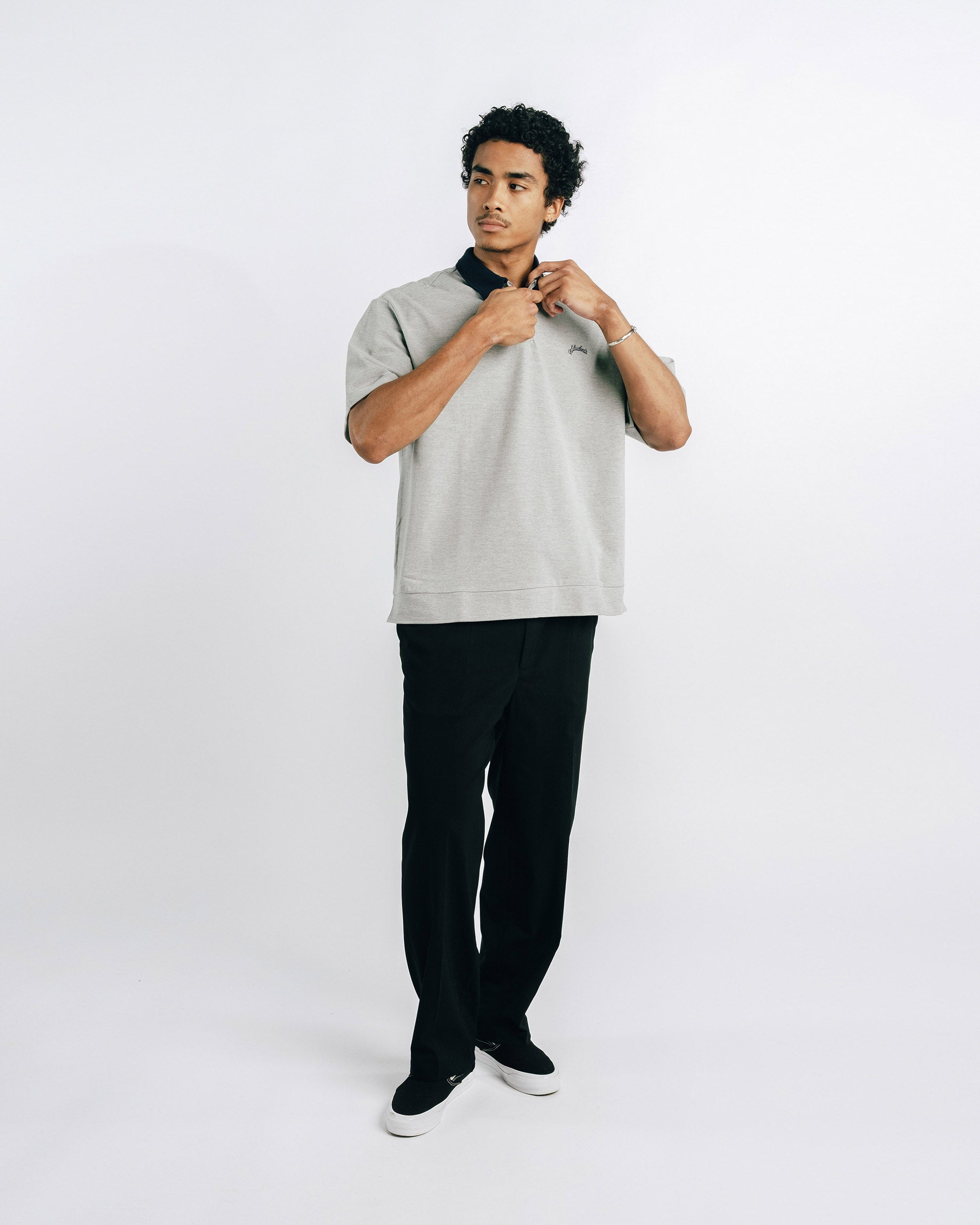 Person wearing a light gray polo shirt with black collar and trim, standing against a white background