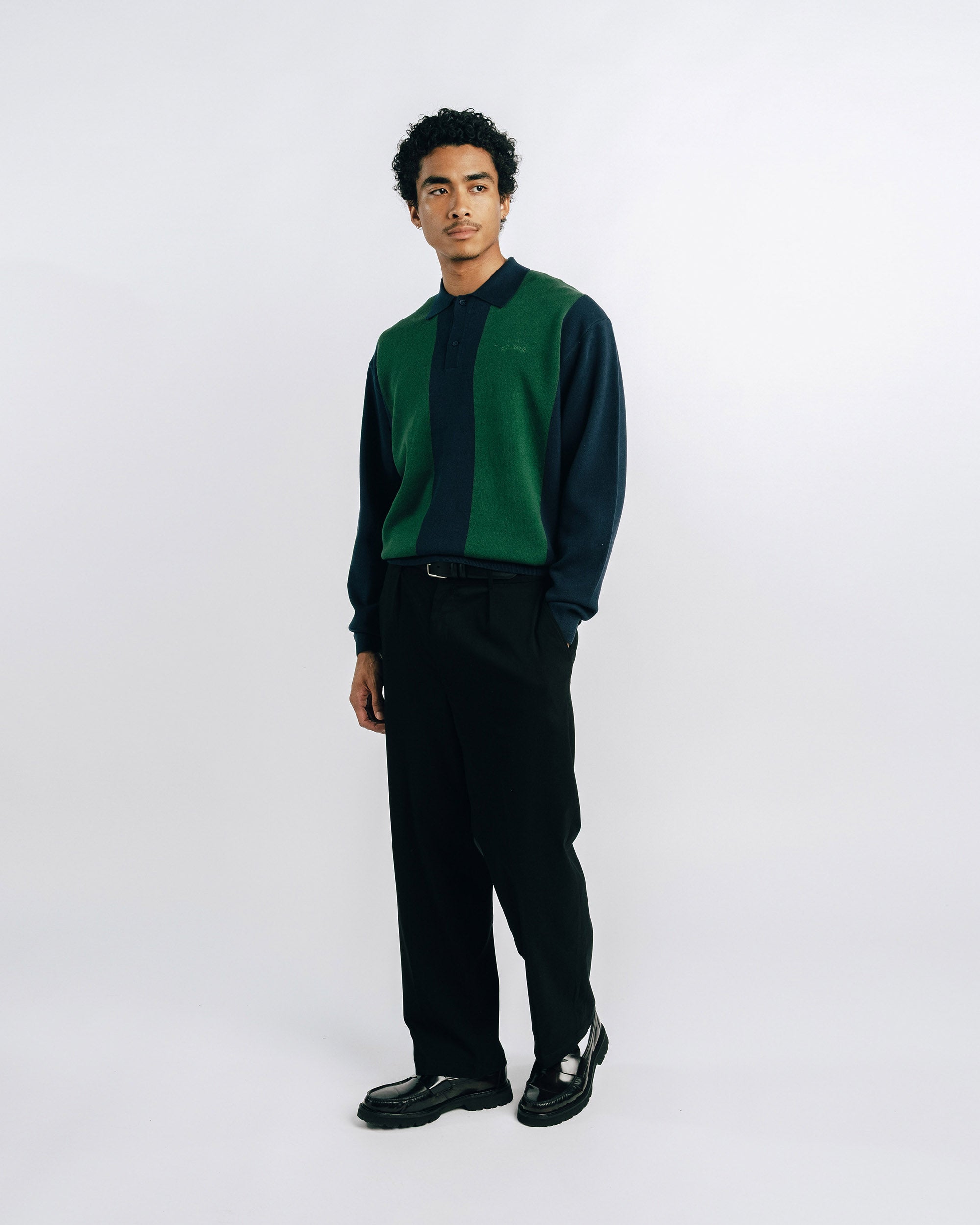 Man wearing a green and black shirt with black pants on a white 