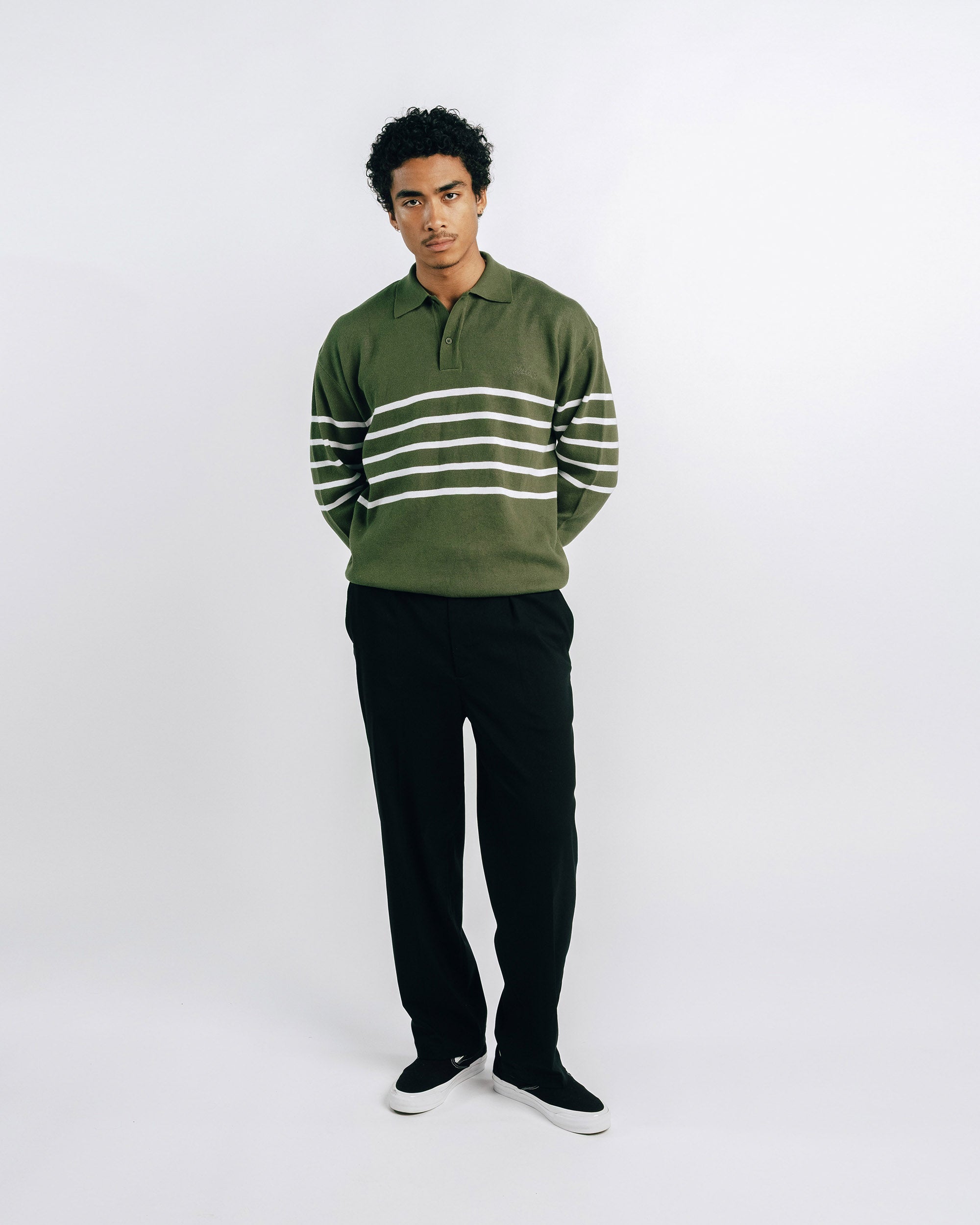 Person wearing a green and white striped sweater with black pants on a white background