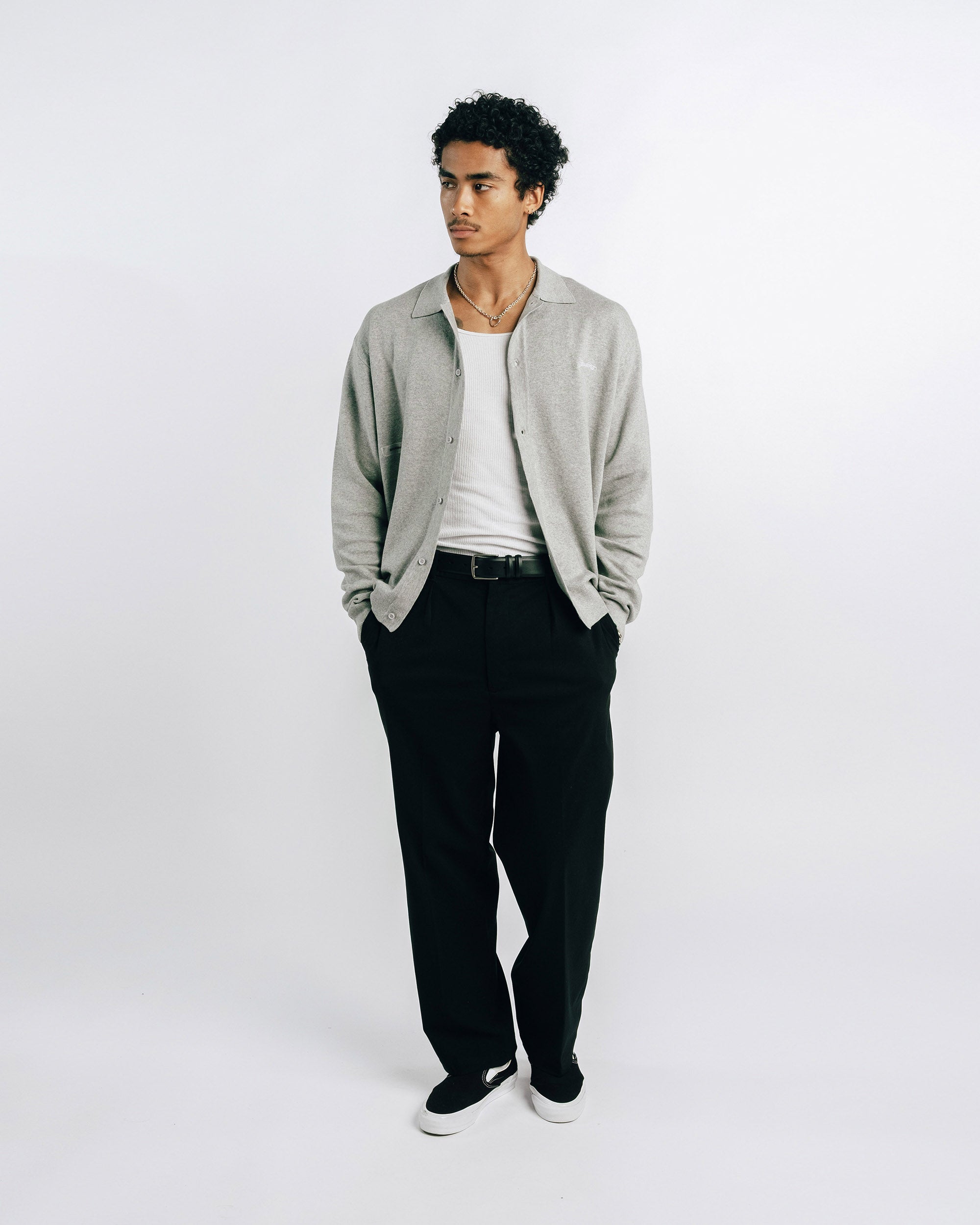 Man wearing a light gray shirt and black pants on a white background