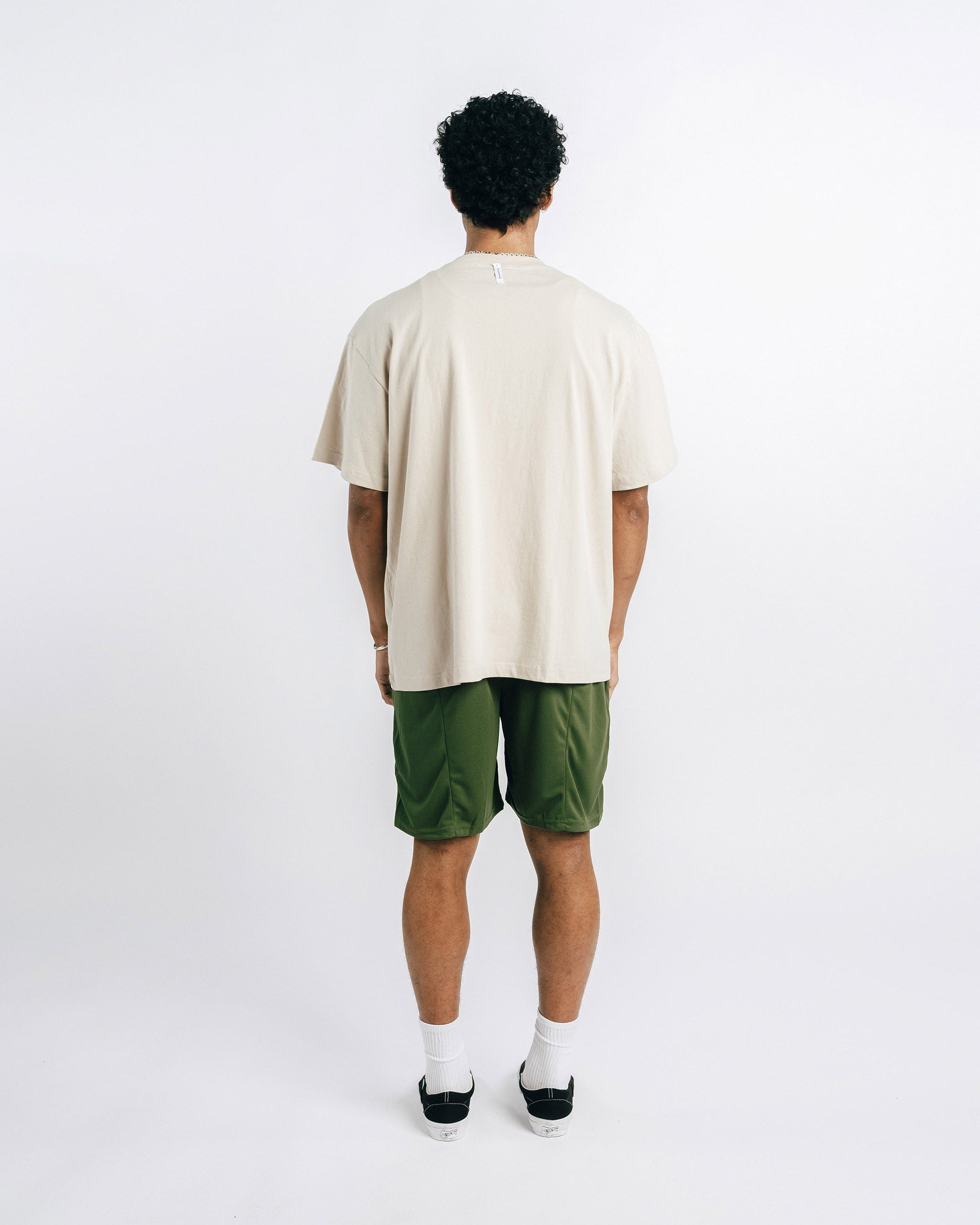 Person wearing a beige t-shirt and green shorts on a white background