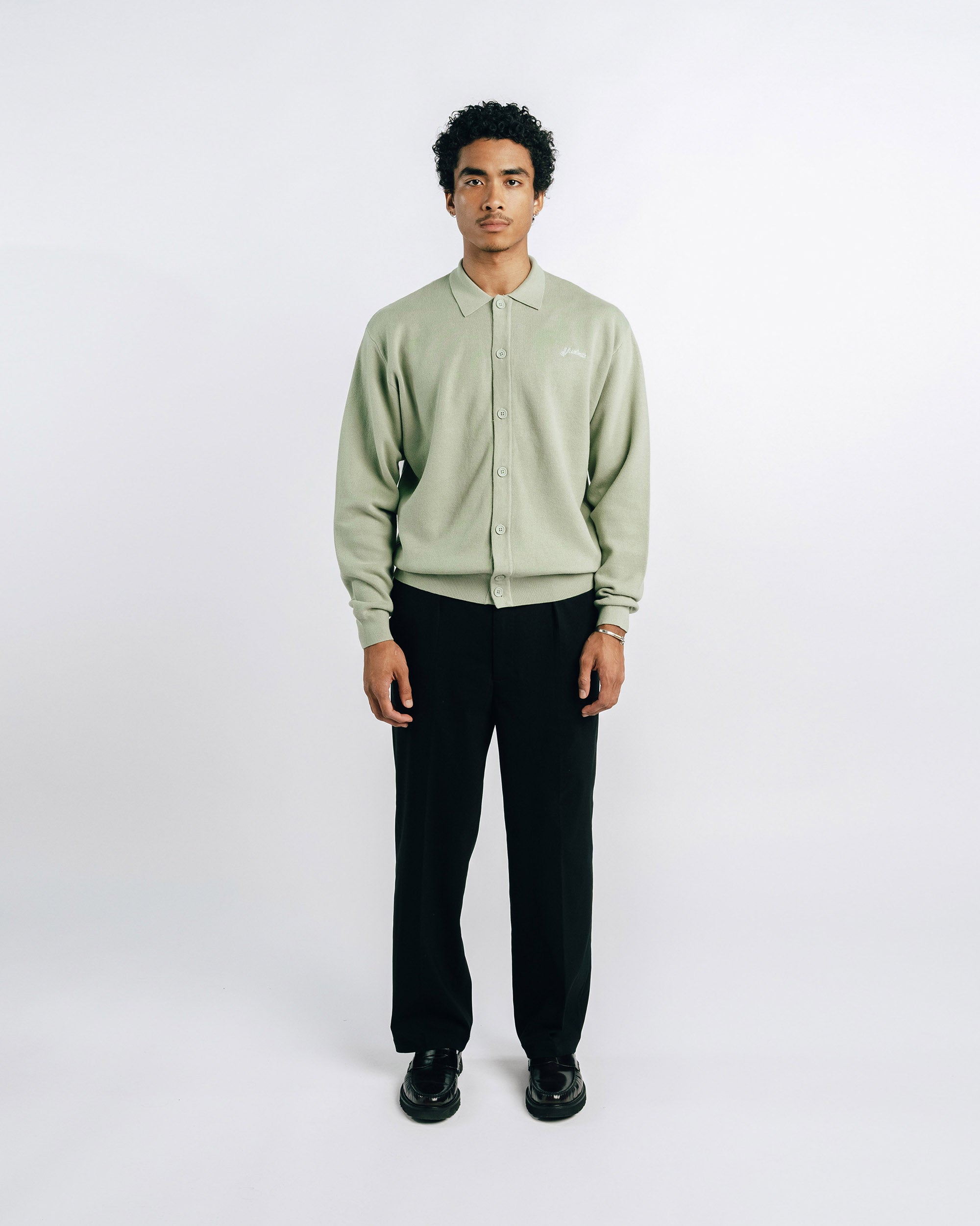 Man wearing a light green shirt and black pants on a white background