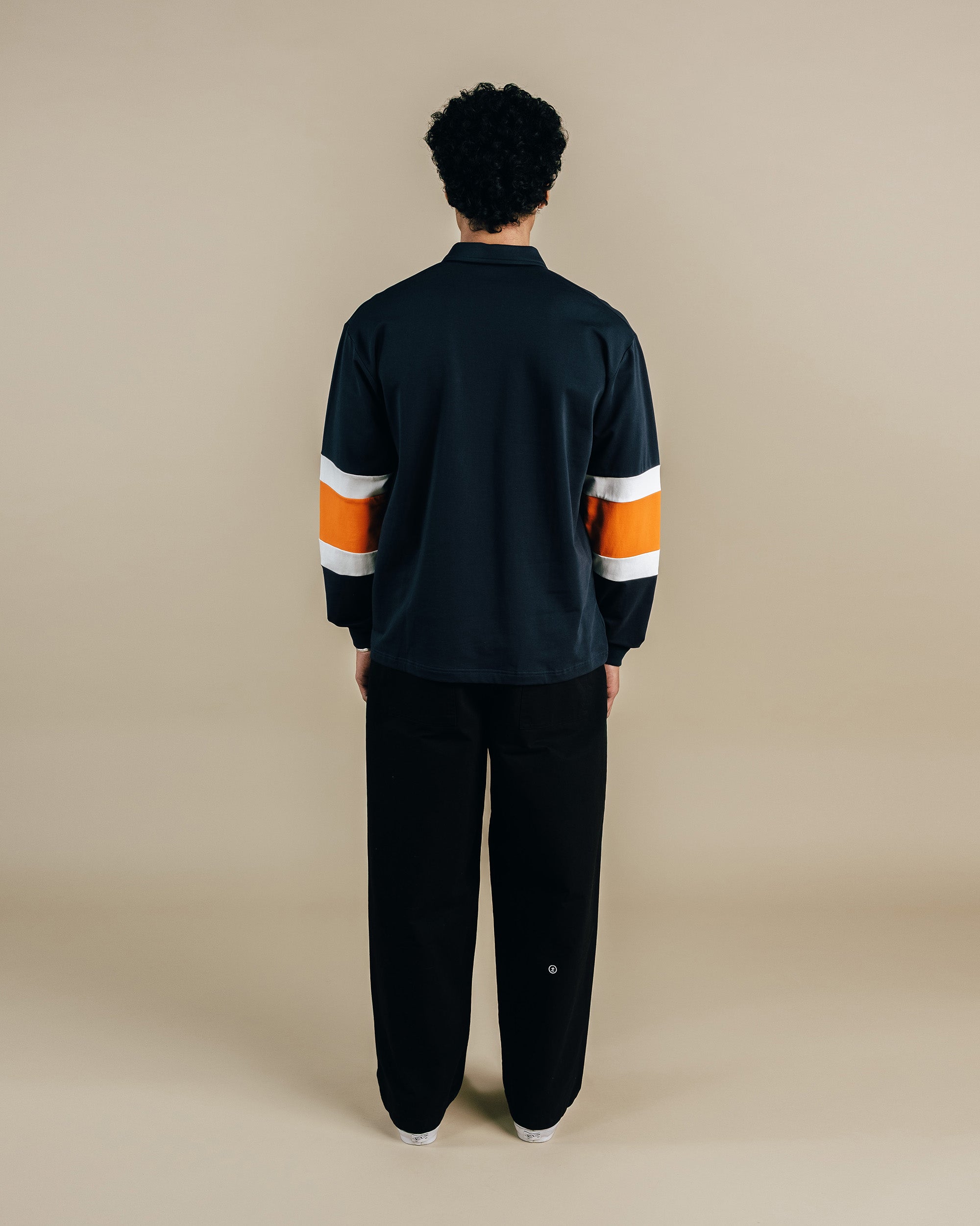 Person wearing a black quarter zip with orange and white stripes on a beige background