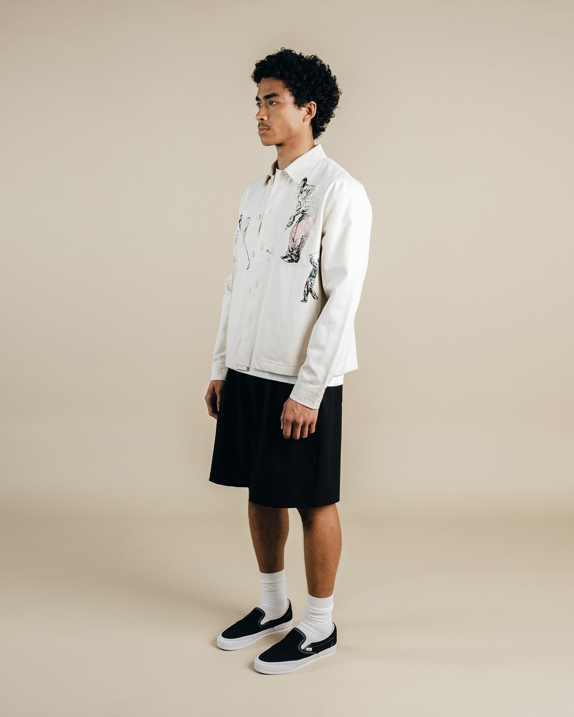 Man wearing a white shirt, black shorts, and black shoes on a beige background