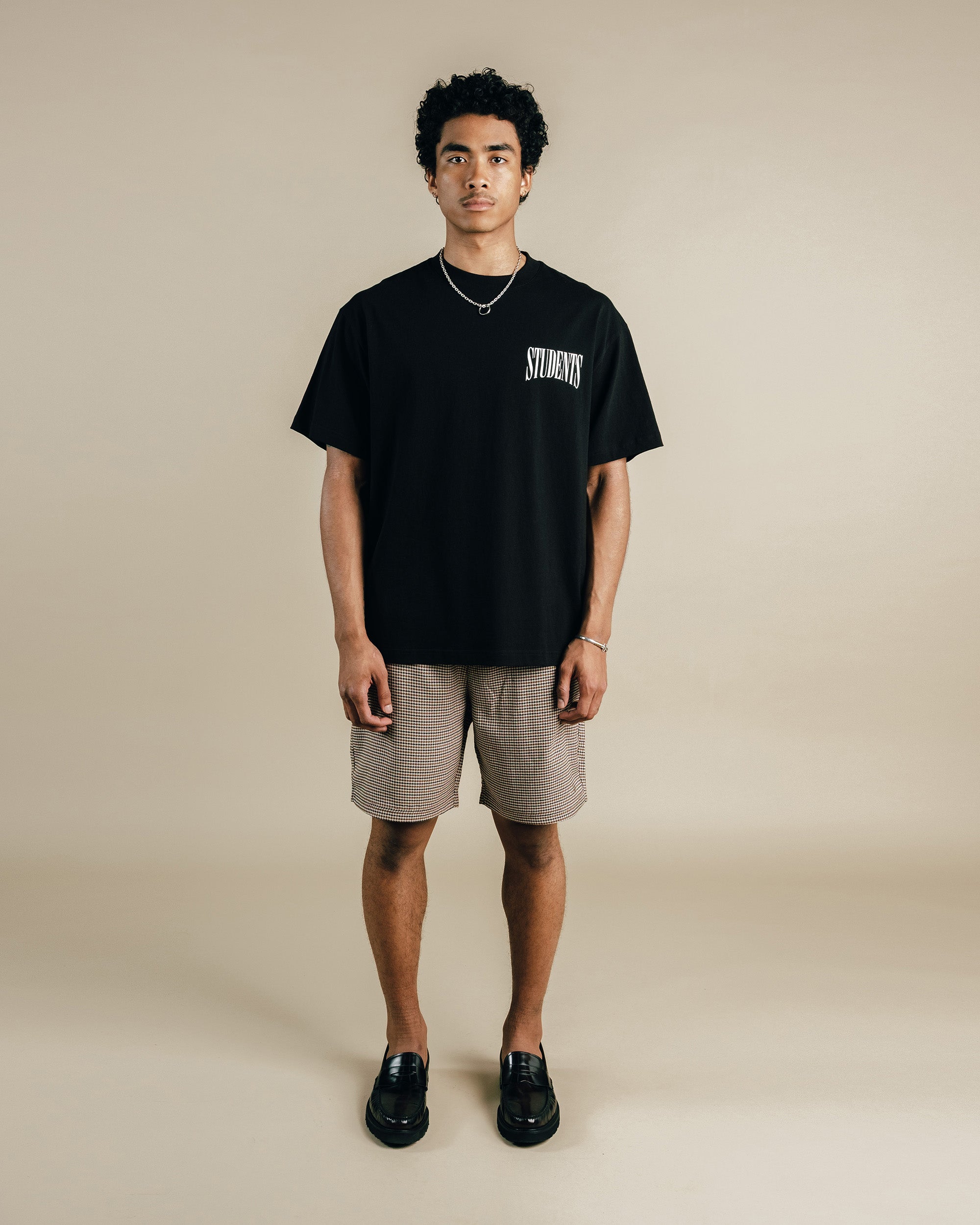 Person wearing a black t-shirt with text and beige shorts on a beige background