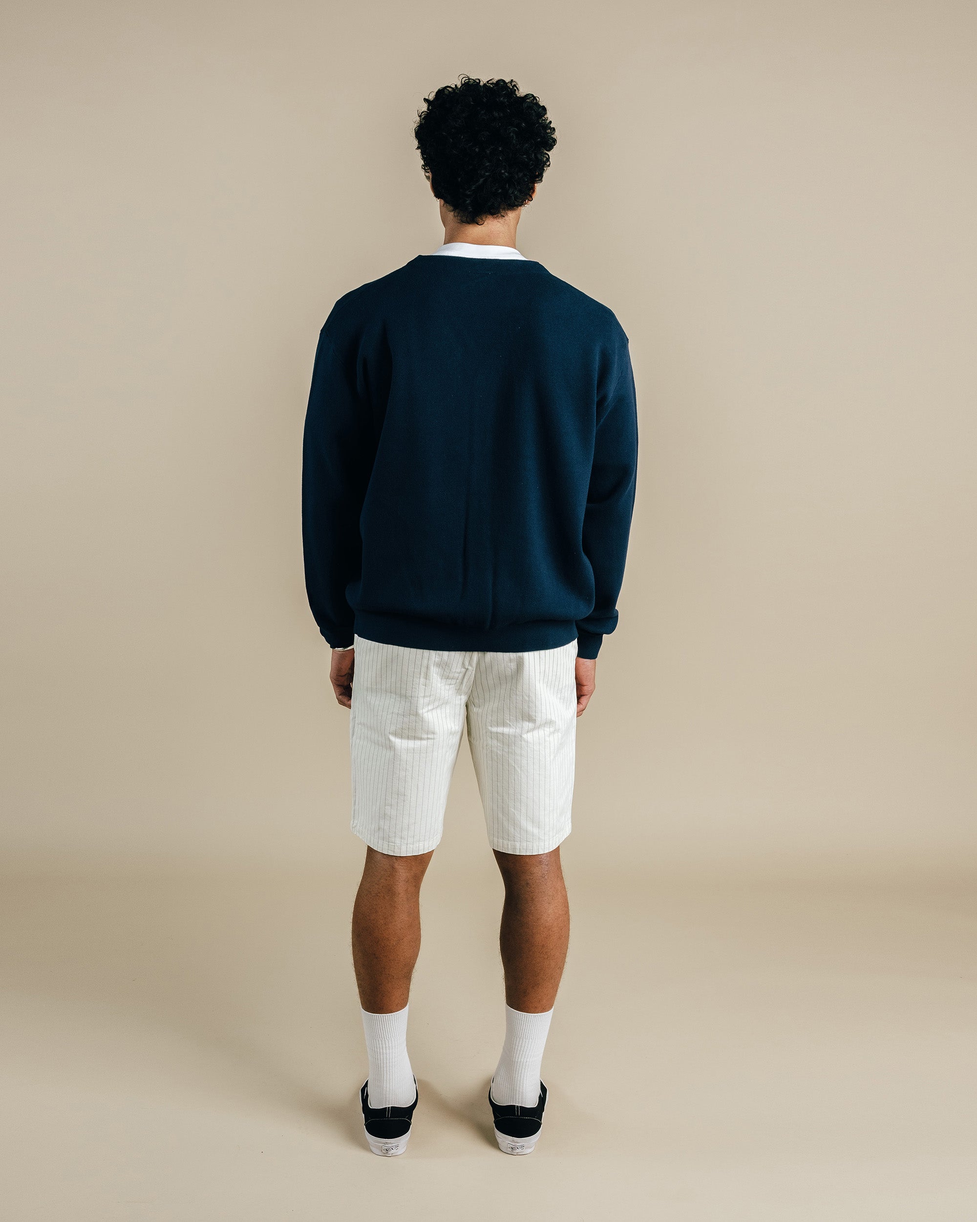 Man wearing a navy sweater and white shorts on a beige background
