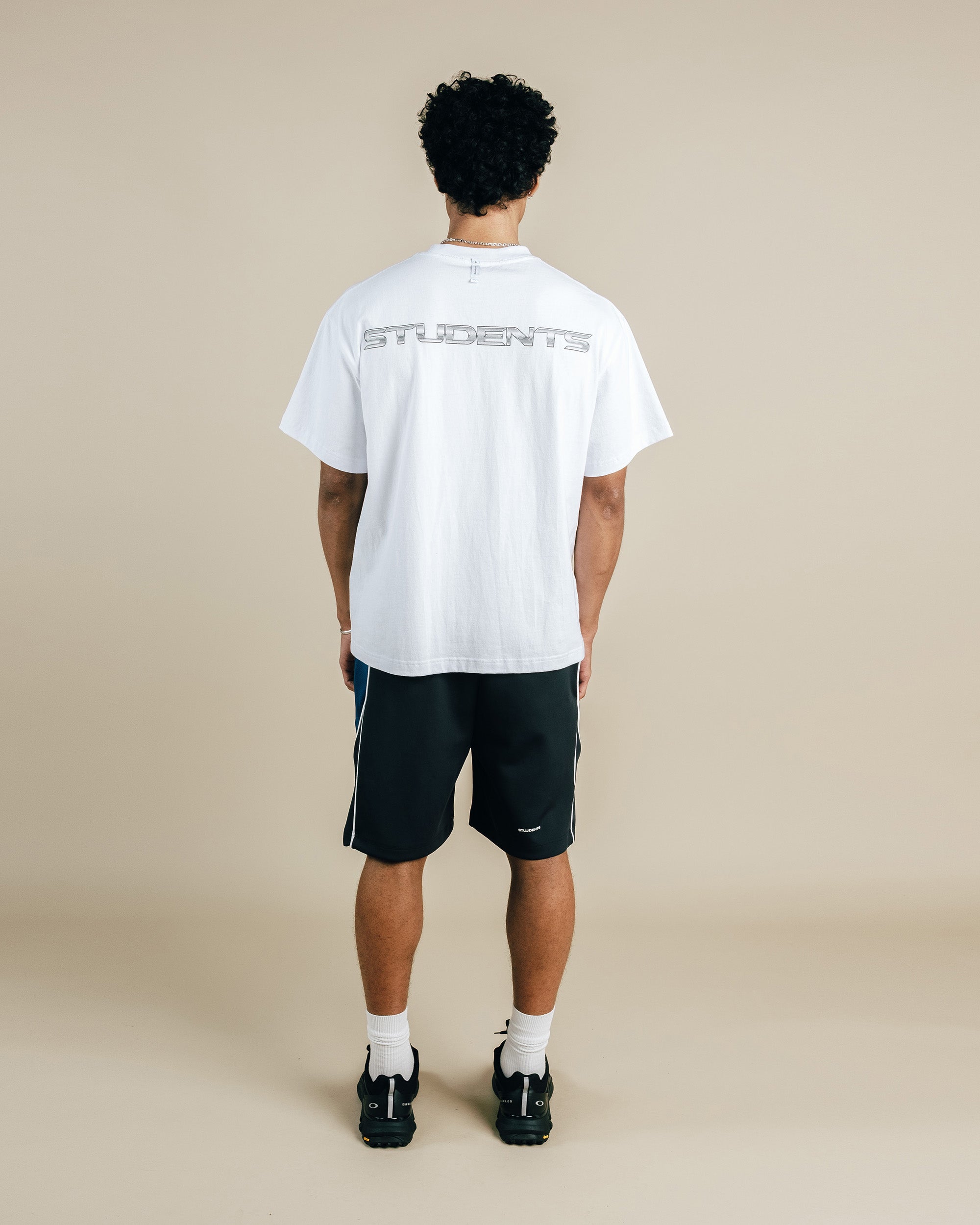 Person wearing a white t-shirt with text on the back and black shorts against a beige background